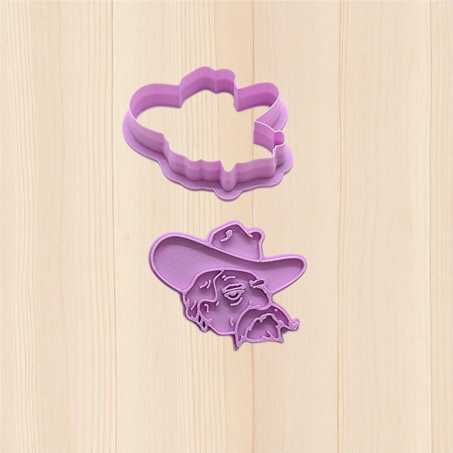 Purple cookie cutter shaped like a face with a hat on a wooden surface