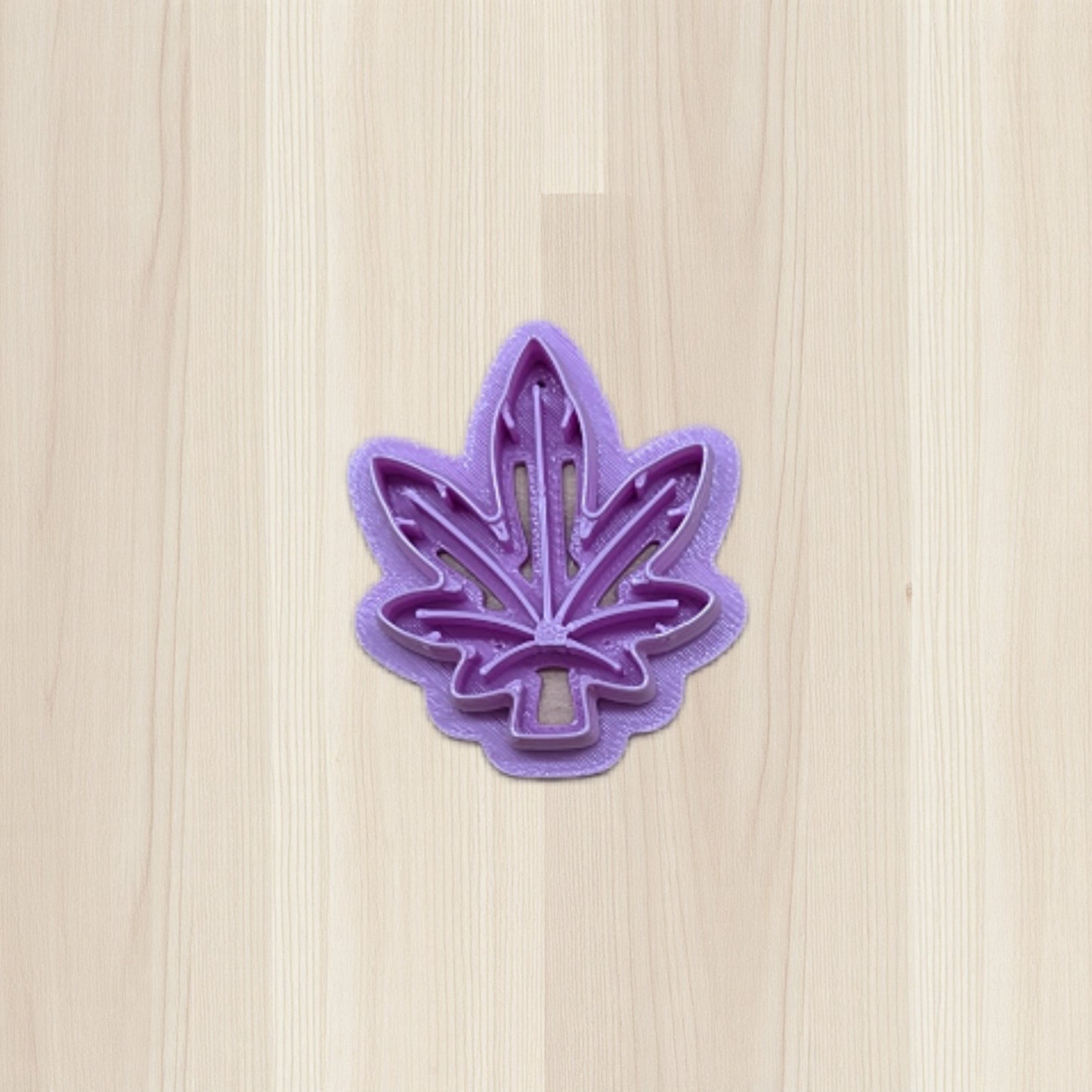 Purple cannabis leaf-shaped cookie cutter on a light wood surface