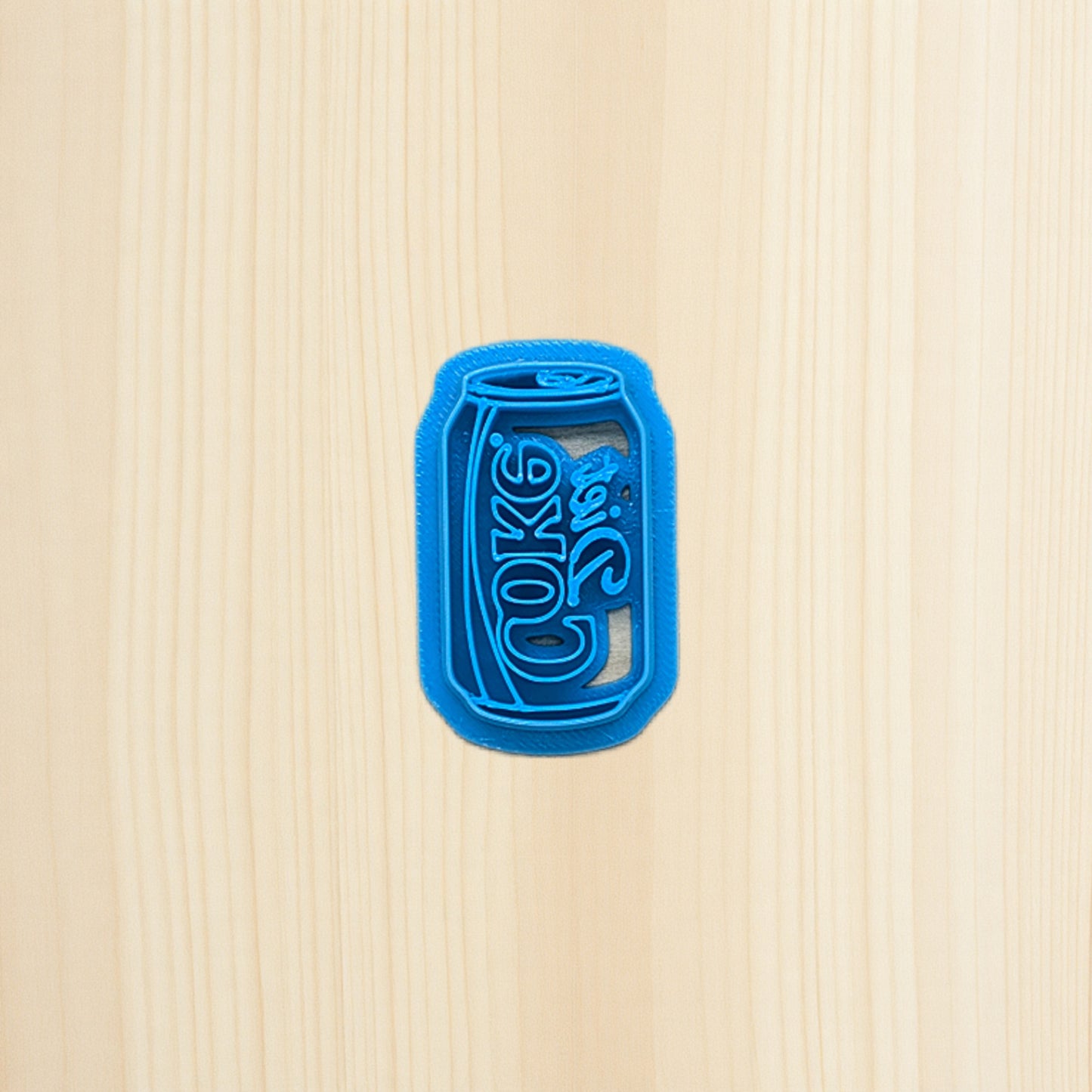 Diet Coke soda pop can cookie cutter laying on wood surface
