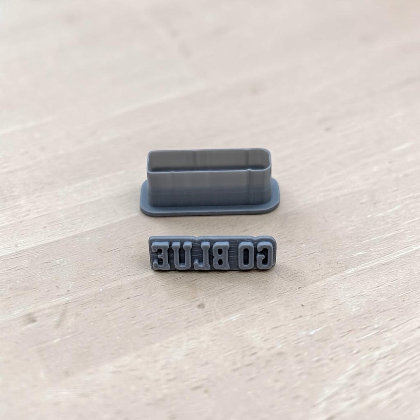 GO BLUE cookie cutter and matching embossing stamp set — gray 3D printed tools on wooden surface for sports‑themed baking or crafts.