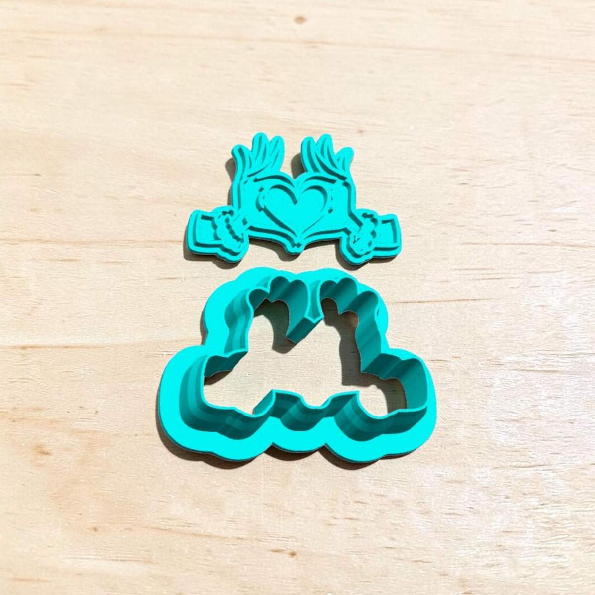 Turquoise 3D-printed Grinch Heart Hands cookie cutter and embossing stamp set featuring furry Christmas hands forming a heart with festive cuffs, photographed on light wood for holiday cookies, polymer clay and fondant crafts.