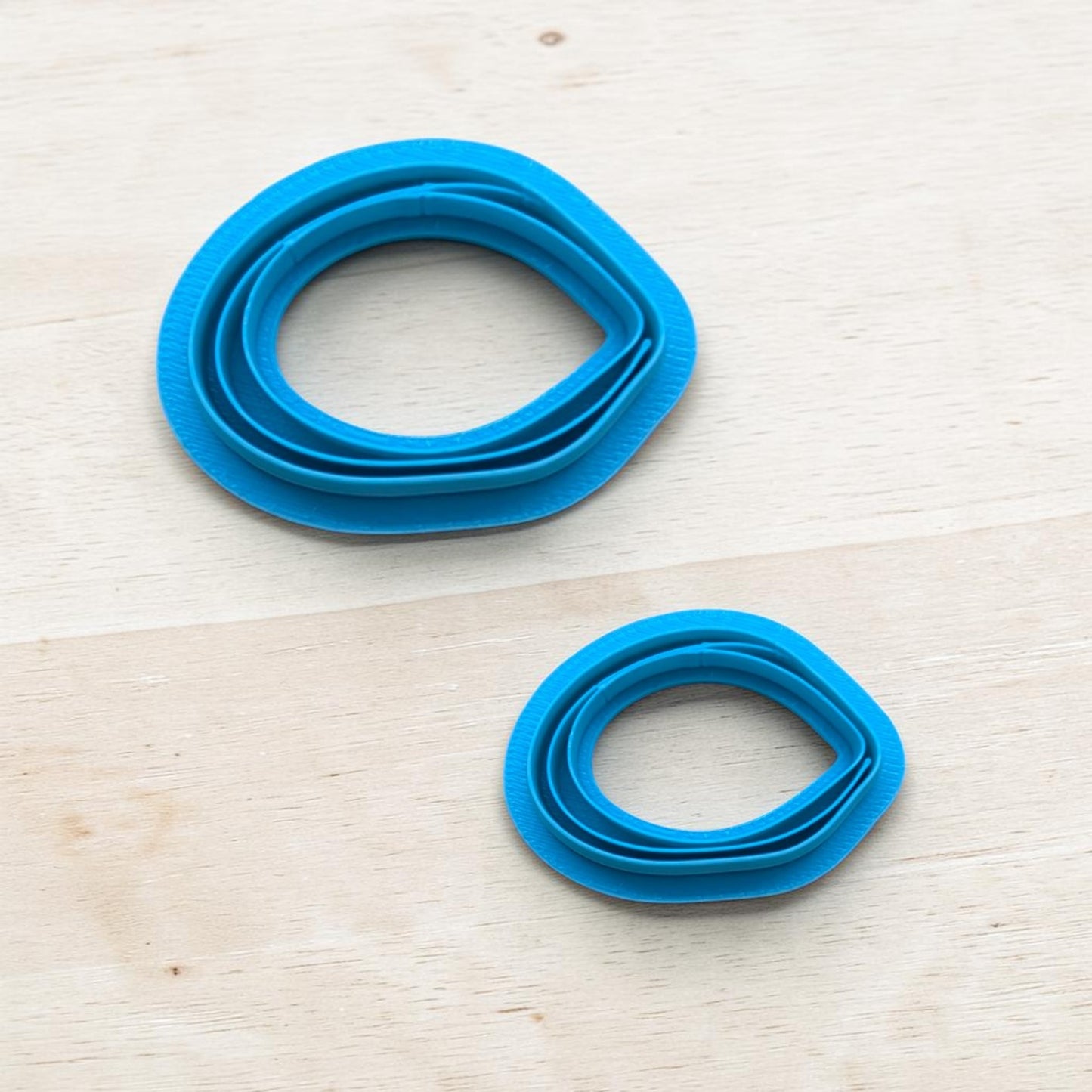 Two blue mussel-shape cookie cutters on a light wooden surface