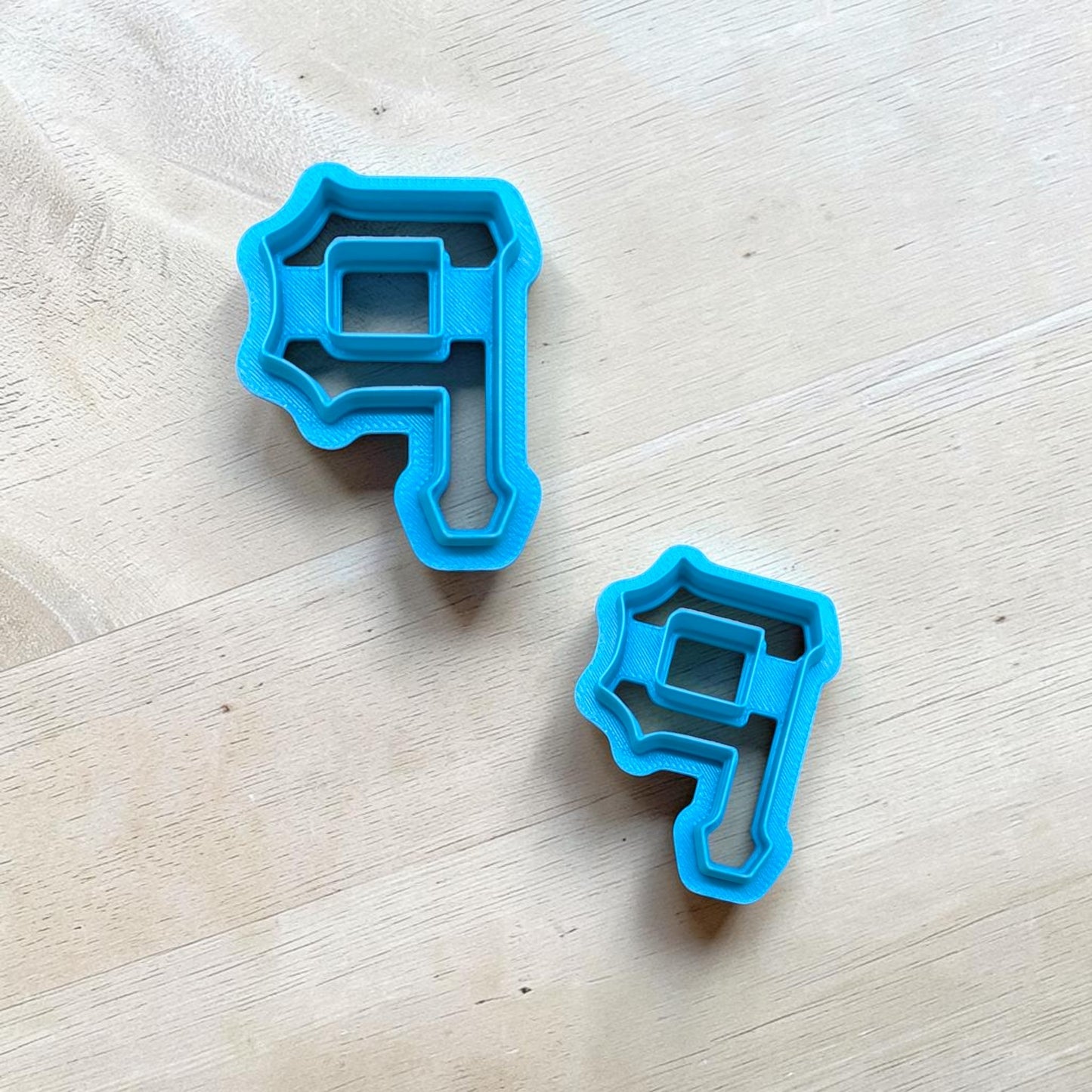Two blue cookie cutters shaped like the Pittsburg Pirates P on a light wooden surface