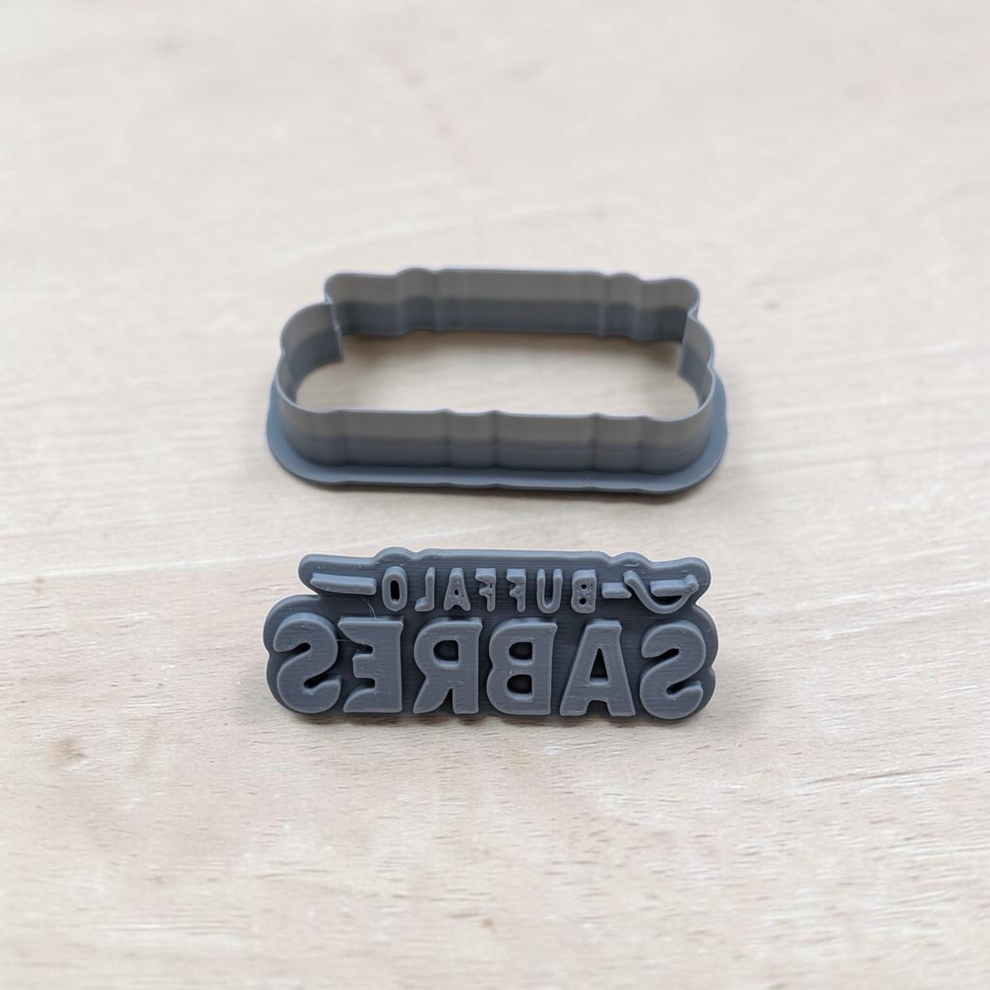 Buffalo Sabres cookie cutter and embossing stamp set – gray 3D printed baking and crafting tools on wooden background.