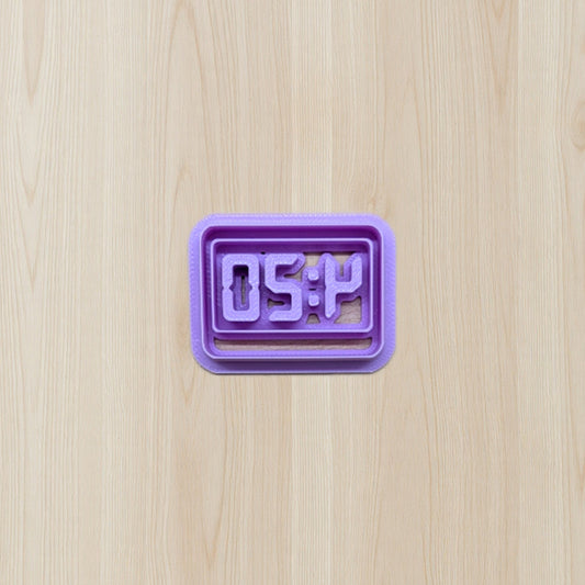 Purple digital clock cookie cutter displaying '4:20' time on a wooden surface