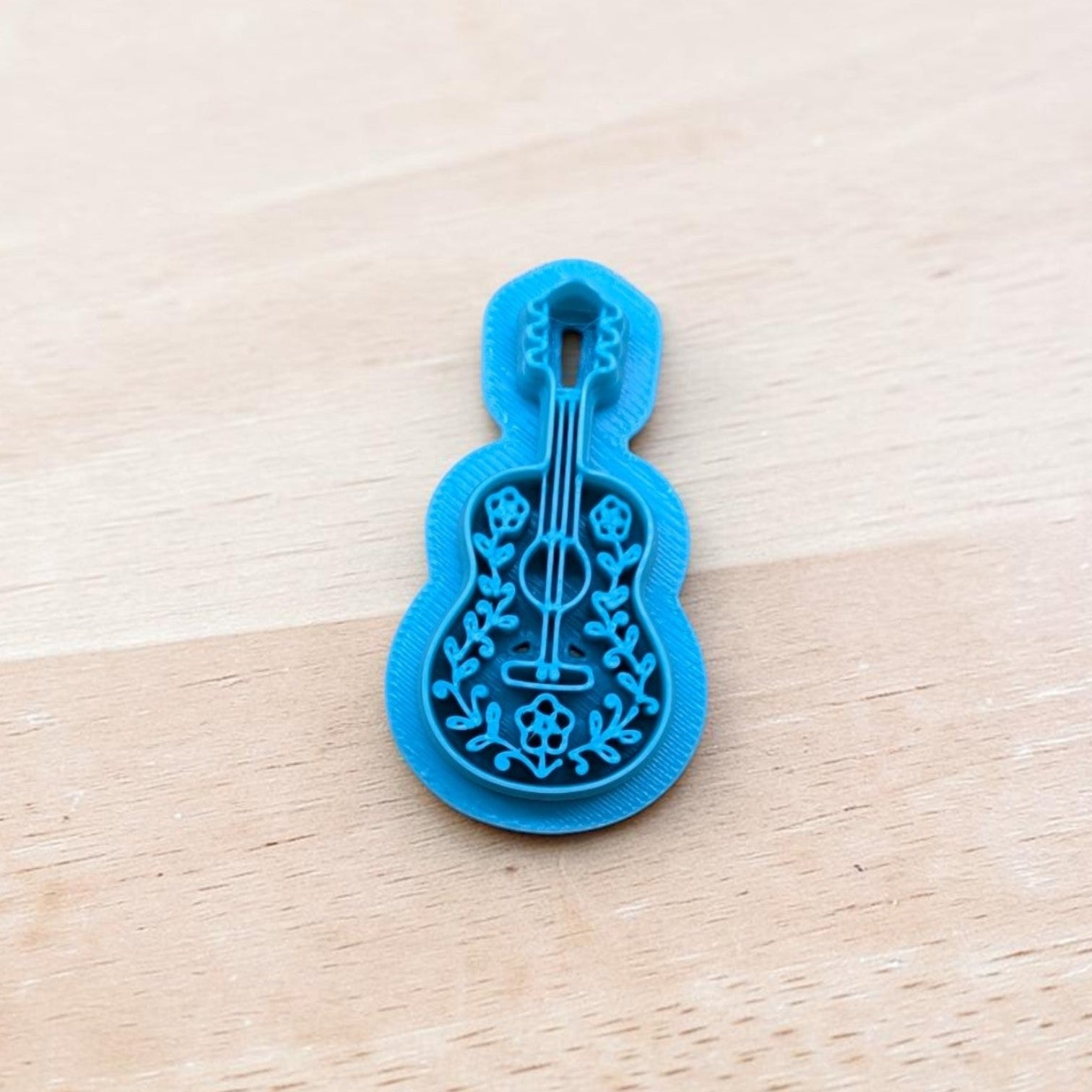 Blue acoustic guitar cookie cutter with floral design for polymer clay, fondant, and pottery crafts on wooden background.