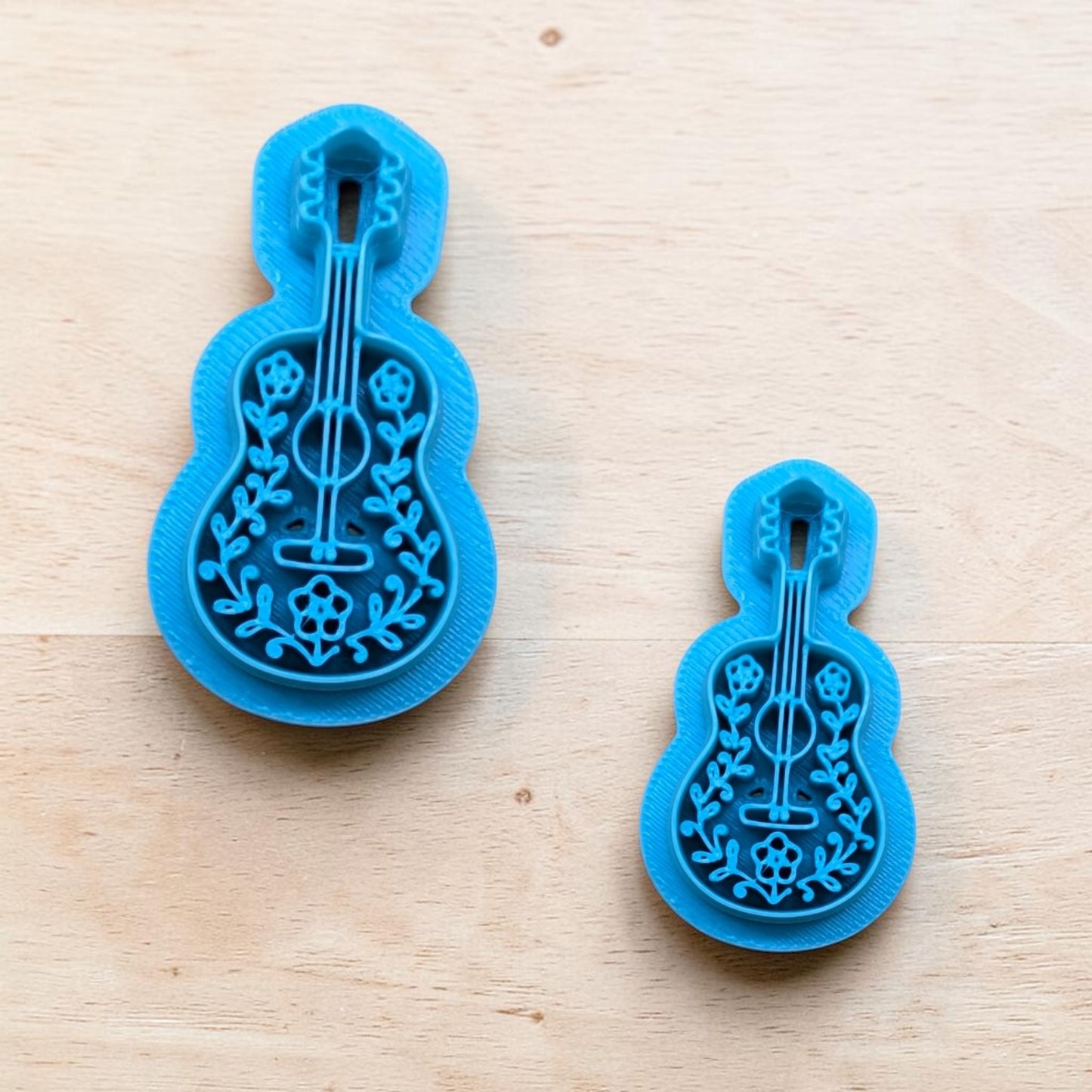 Two blue acoustic guitar cookie cutters with floral detailing in different sizes for polymer clay, fondant, and pottery crafts on wooden surface.