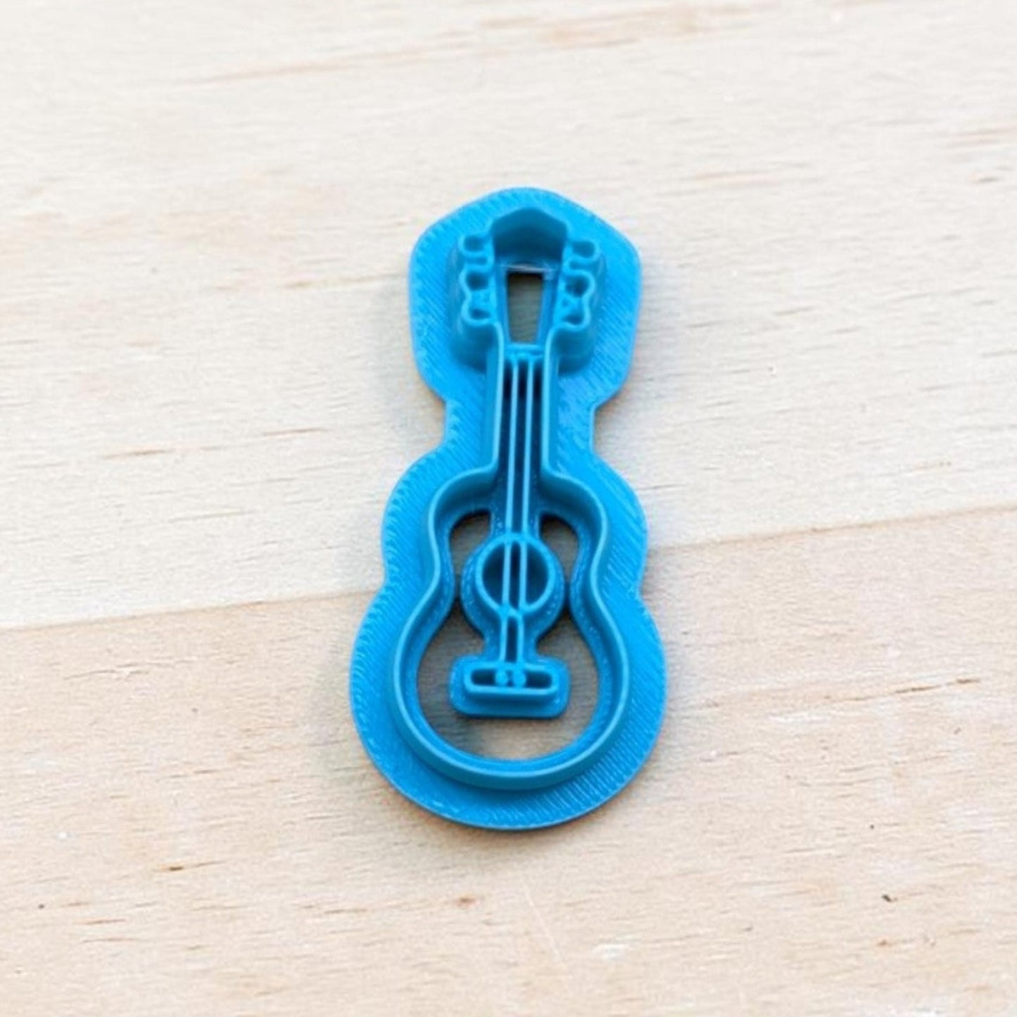 Blue acoustic guitar cookie cutter for polymer clay, fondant, pottery, and ceramic crafts on wooden background.