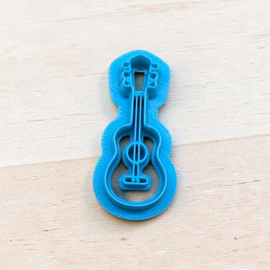 Blue acoustic guitar cookie cutter for polymer clay, fondant, pottery, and ceramic crafts on wooden background.