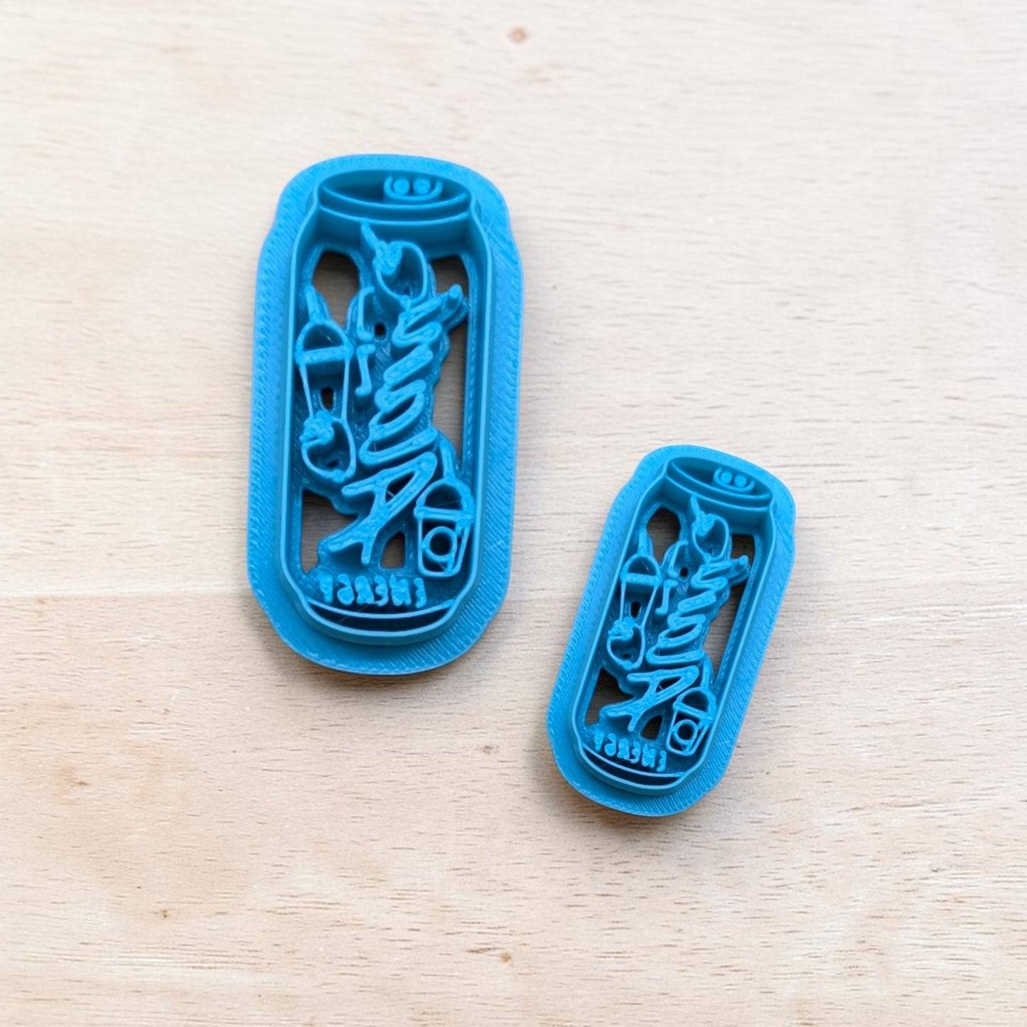 Two blue 3D‑printed Alani Nu energy drink can cookie cutters in large and small sizes displayed on light wood surface — ideal for baking and crafting.