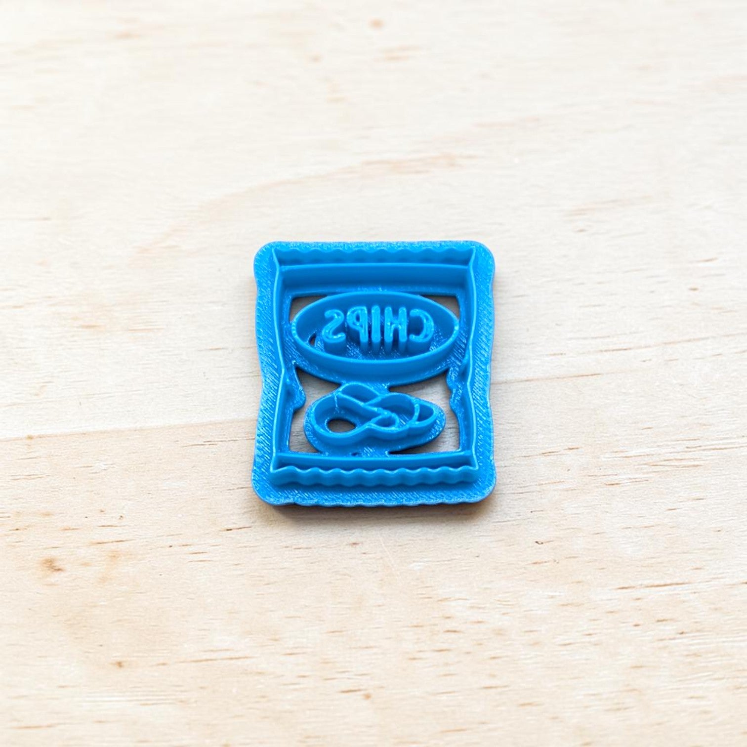 Blue cookie cutter shaped like a bag of chips on a light wood surface