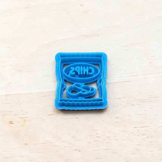 Blue cookie cutter shaped like a bag of chips on a light wood surface