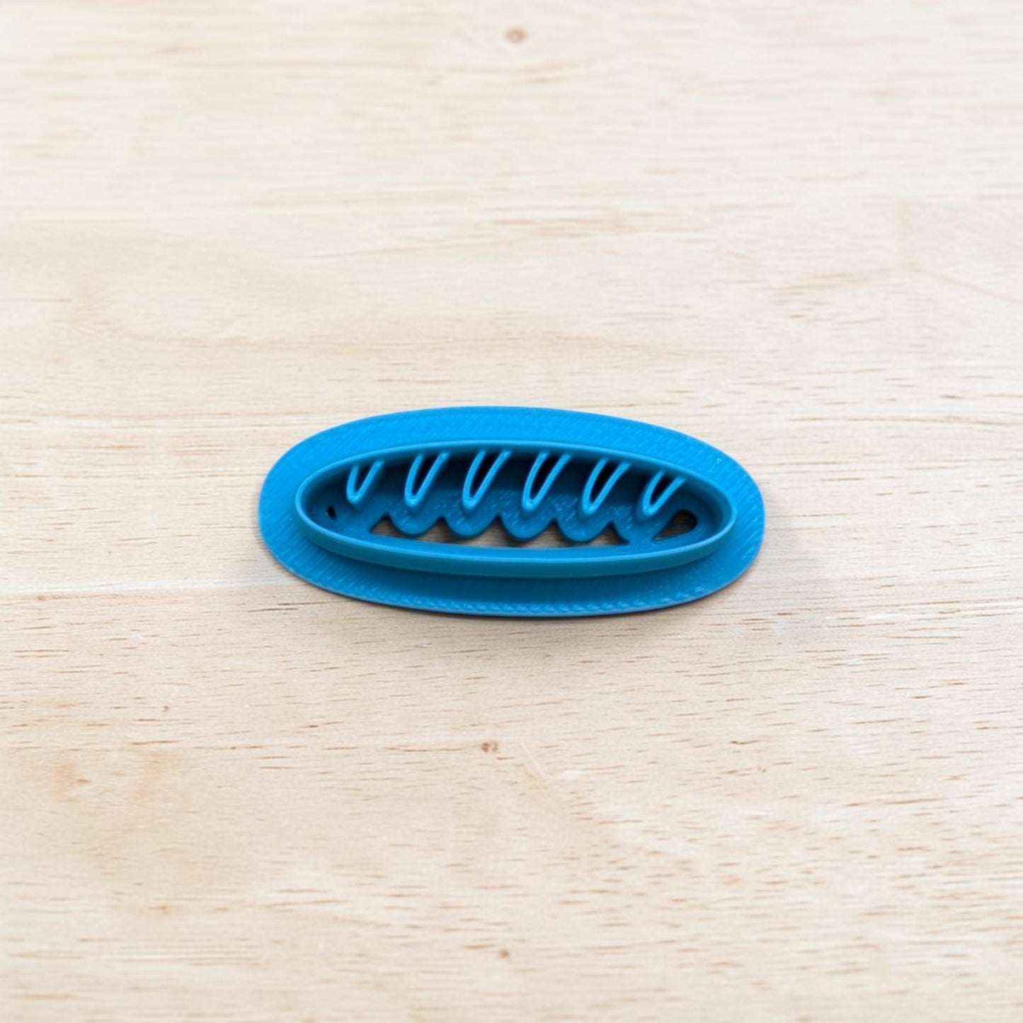 Blue plastic baguette bread-shaped cookie cutter on a light wooden surface