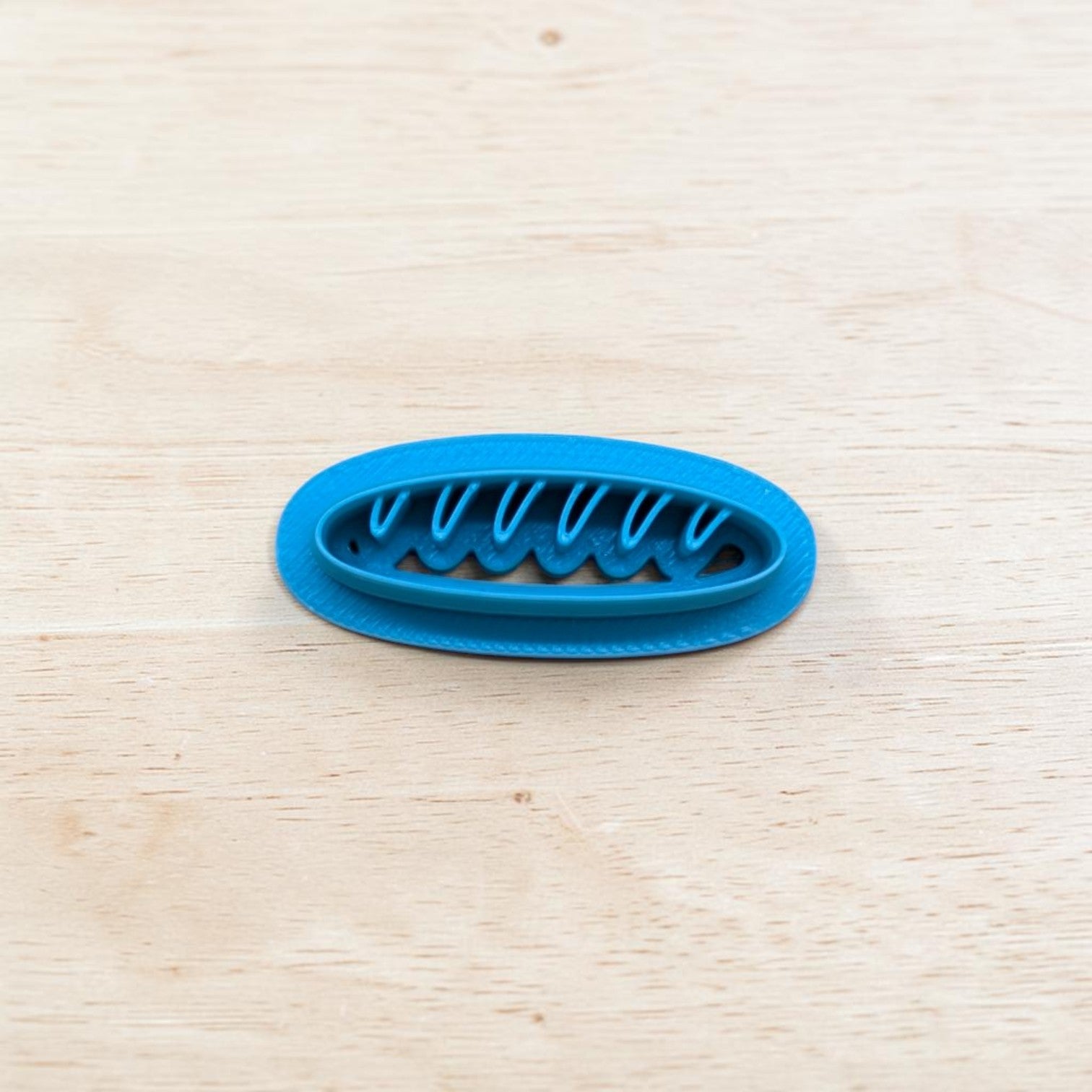 Blue plastic baguette bread-shaped cookie cutter on a light wooden surface