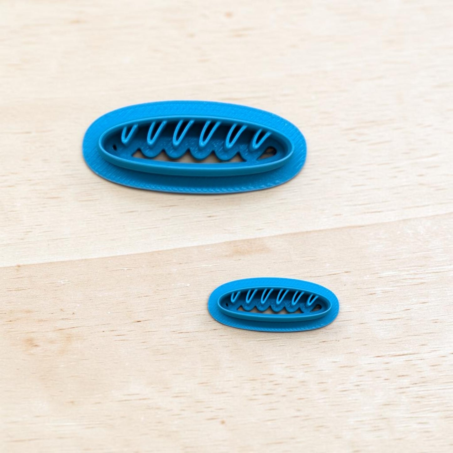 Two blue oval cookie cutters with wavy edge design on a light wooden surface.