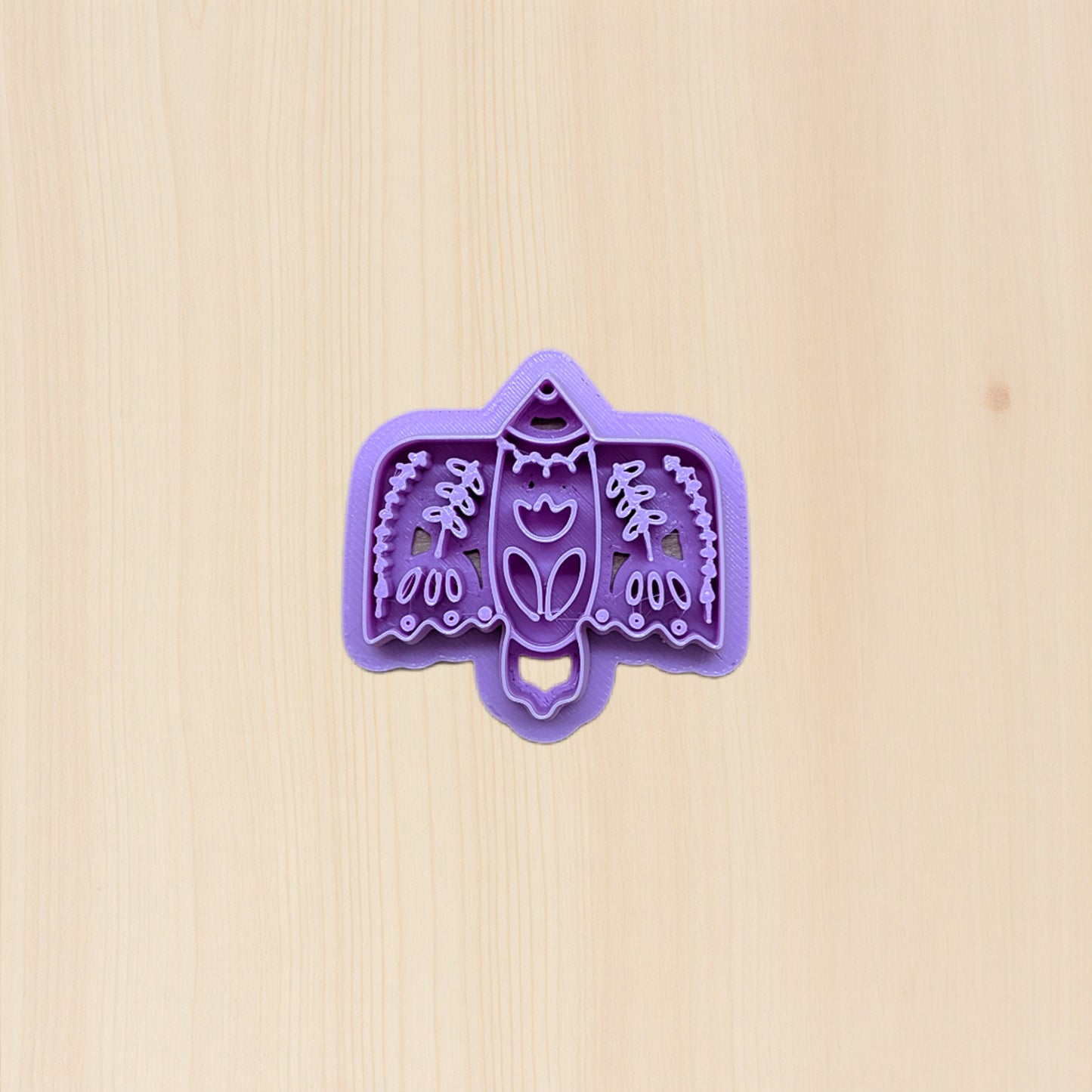Purple bird-shaped cookie cutter with folk art design on a beige background
