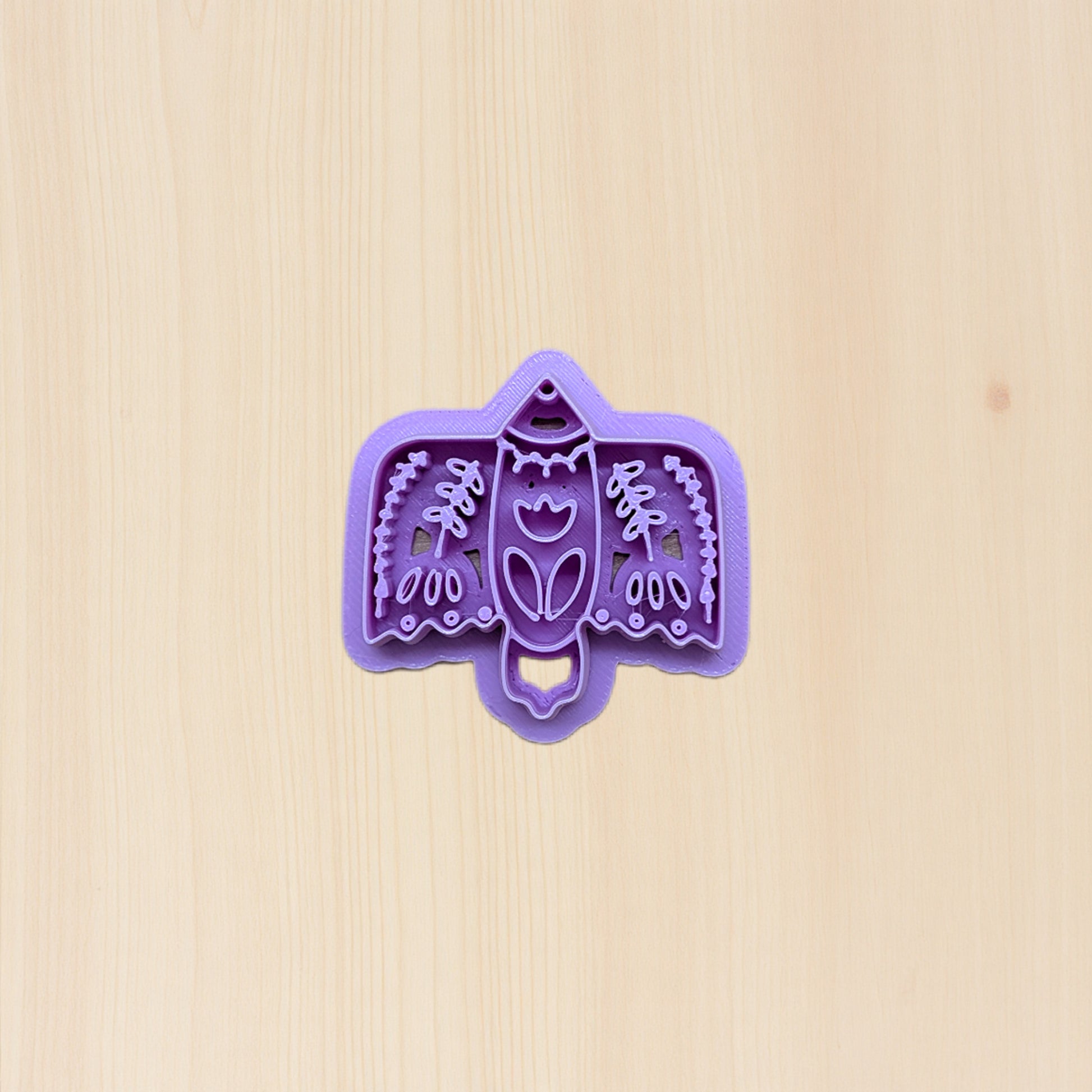 Purple bird-shaped cookie cutter with folk art design on a beige background