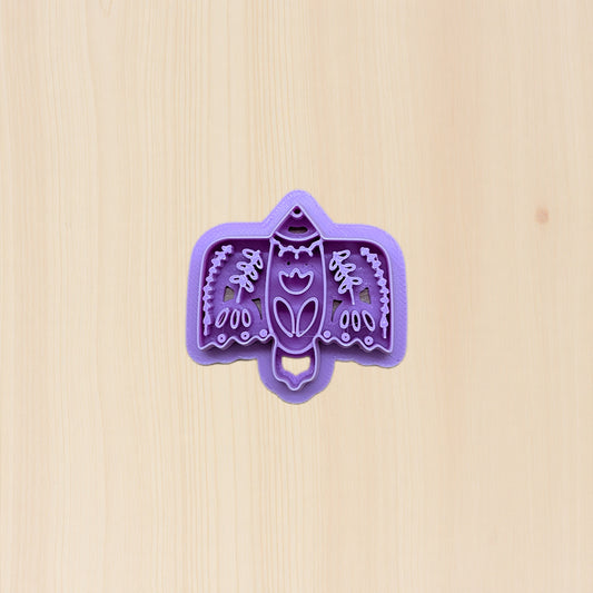 Purple bird-shaped cookie cutter with folk art design on a beige background