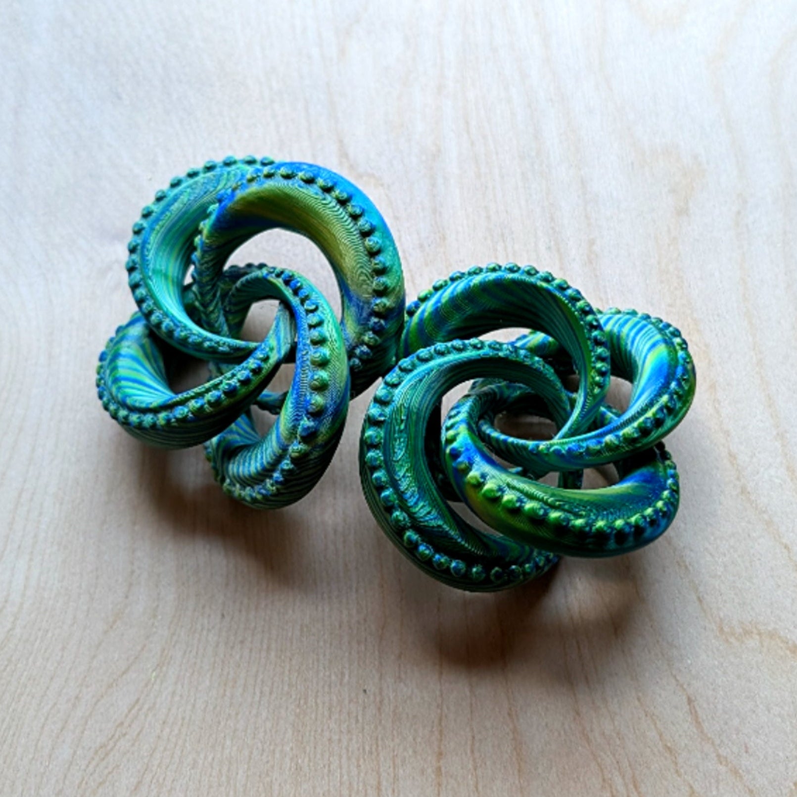 Pair of green spiral earrings on a light wood surface