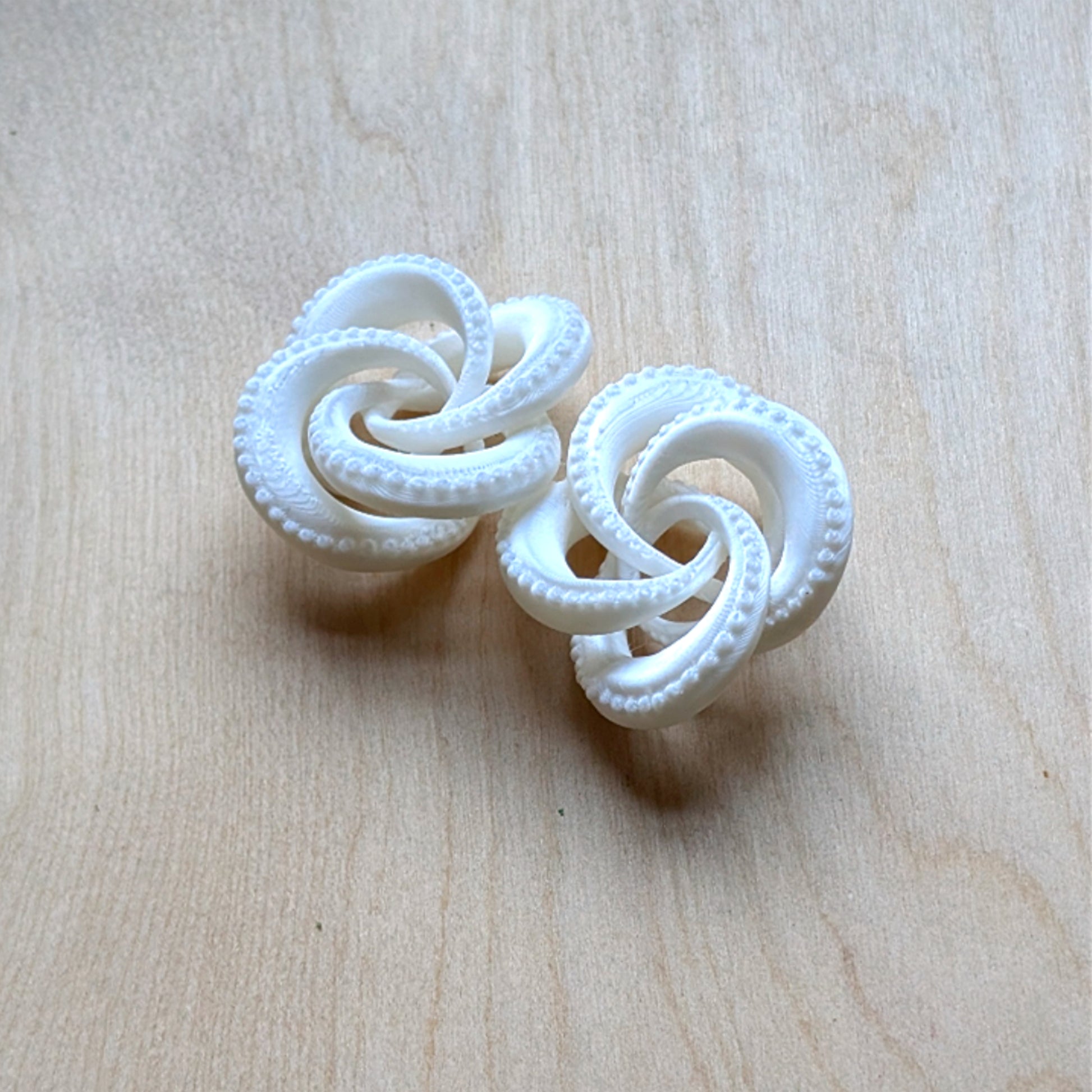 Pair of white knotted earrings on a light wood surface
