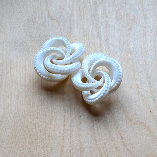 Pair of white knotted earrings on a light wood surface