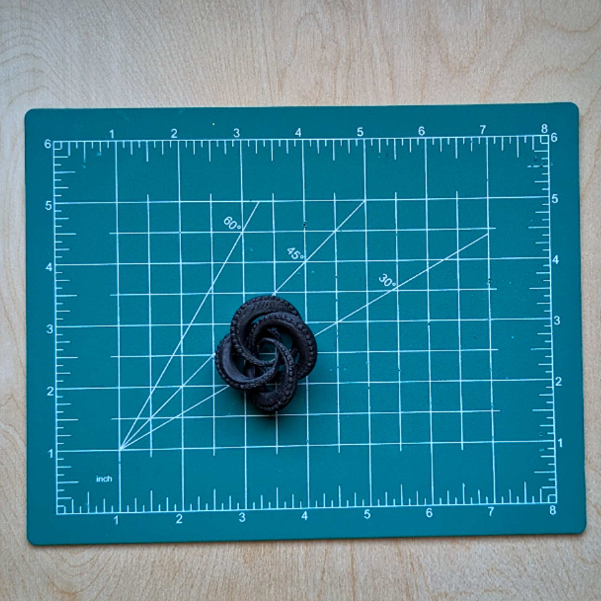 Black flower-shaped object on a teal cutting mat with grid lines.