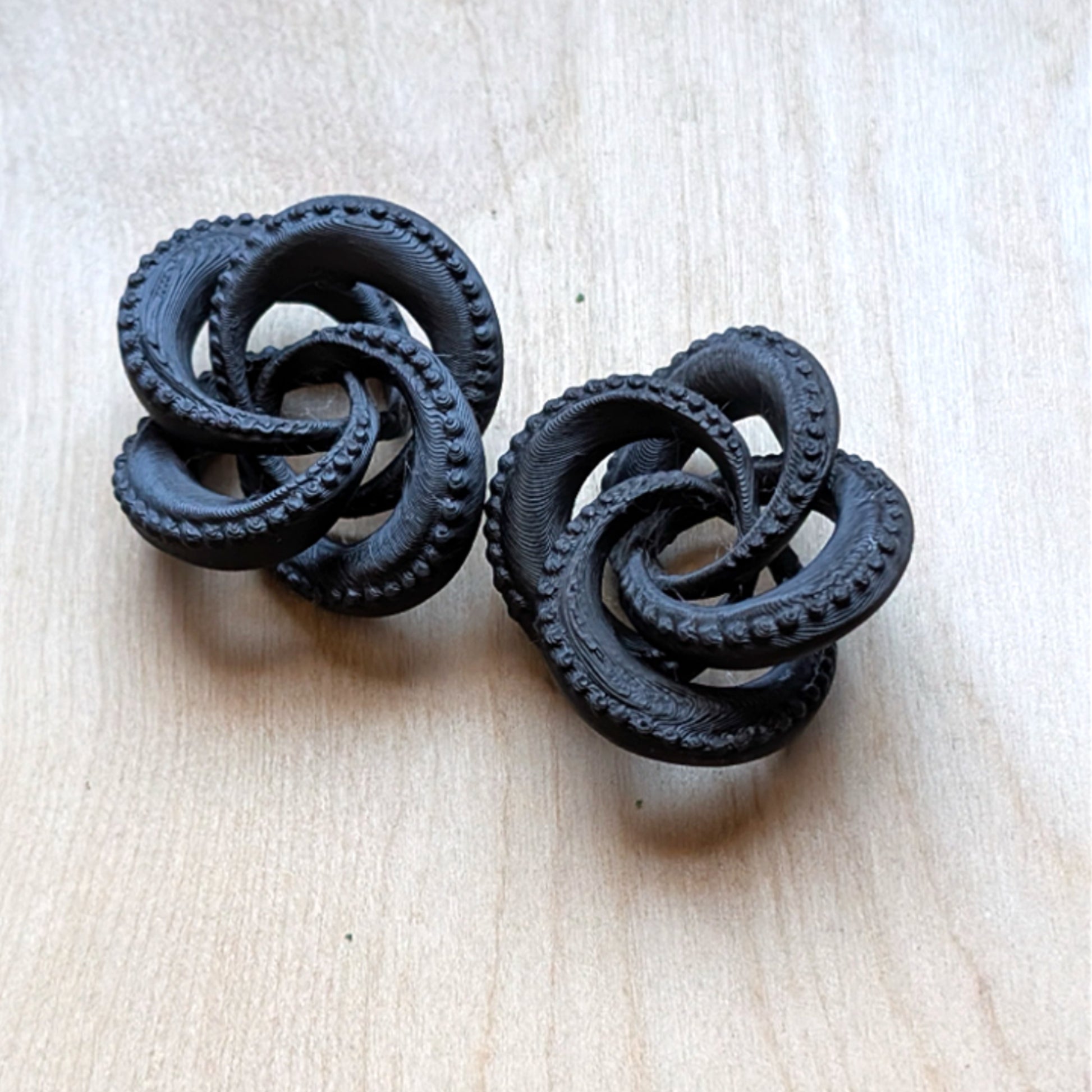 Pair of black knot earrings on a light beige background