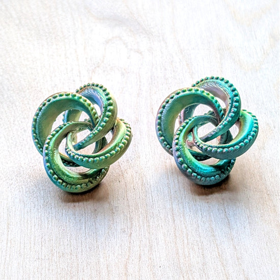 Pair of green knotted earrings on a light wooden surface