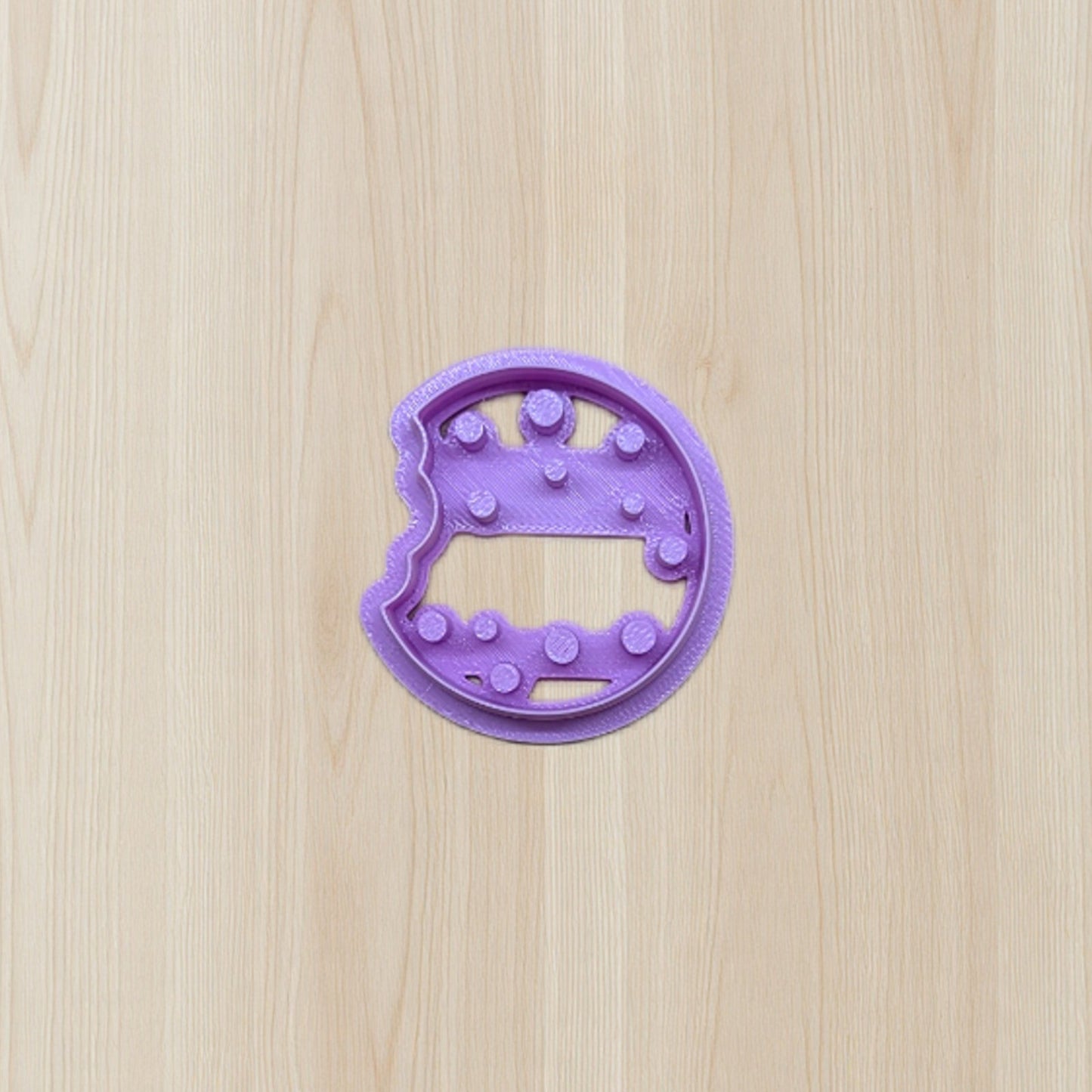 Purple cookie cutter shaped like a dinosaur on a wooden surface