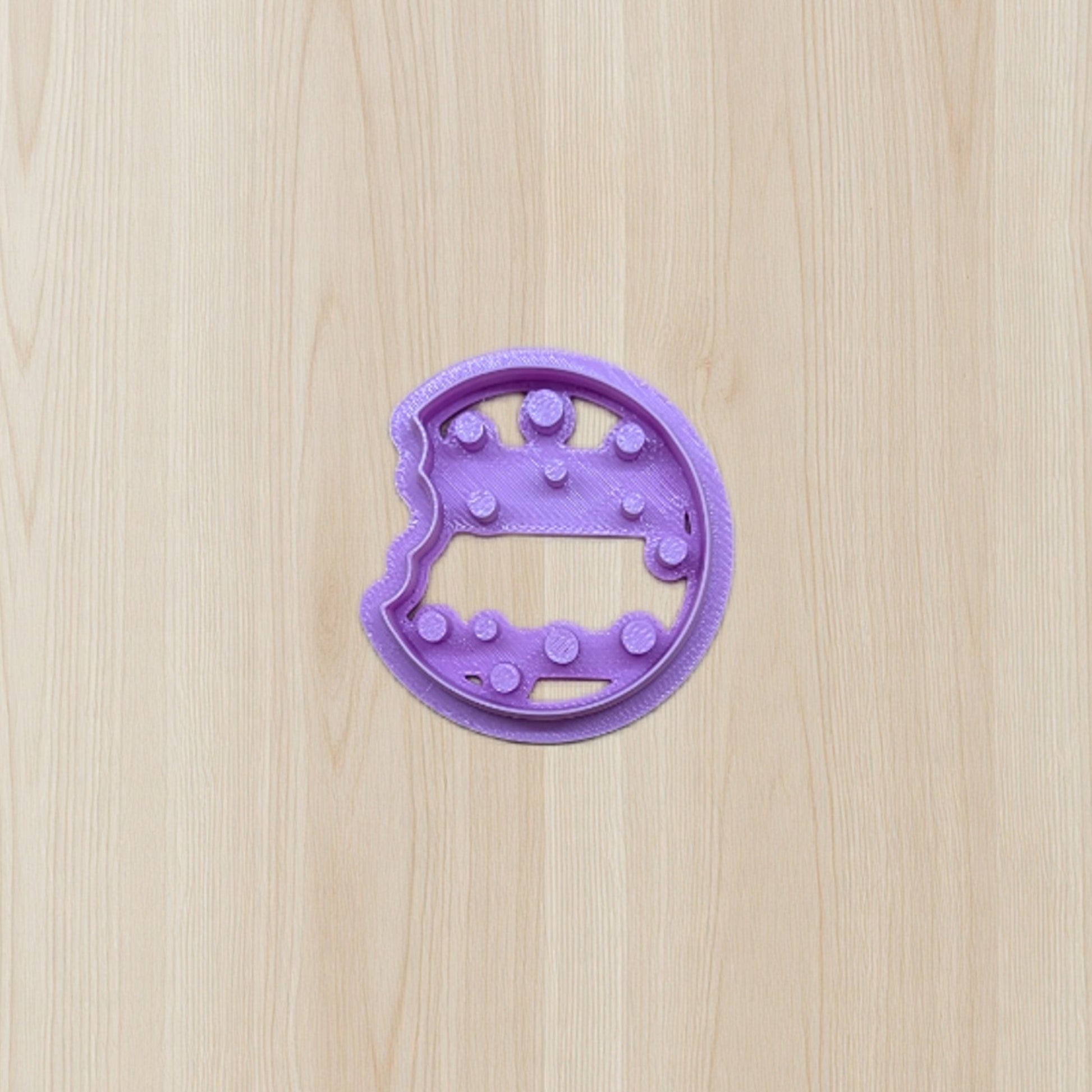 Purple cookie cutter shaped like a dinosaur on a wooden surface