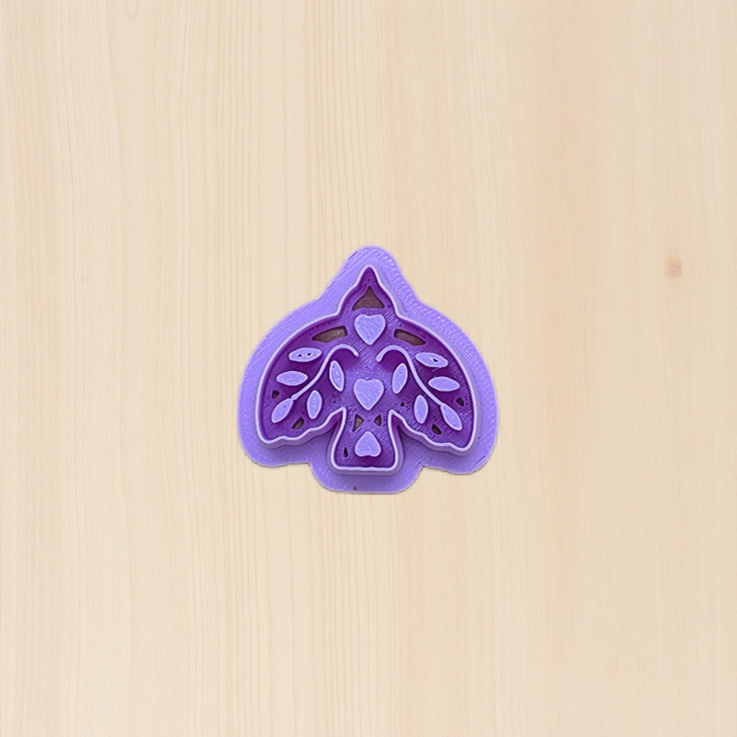 Purple boho bird cookie cutter with folk art design on a birchwood background