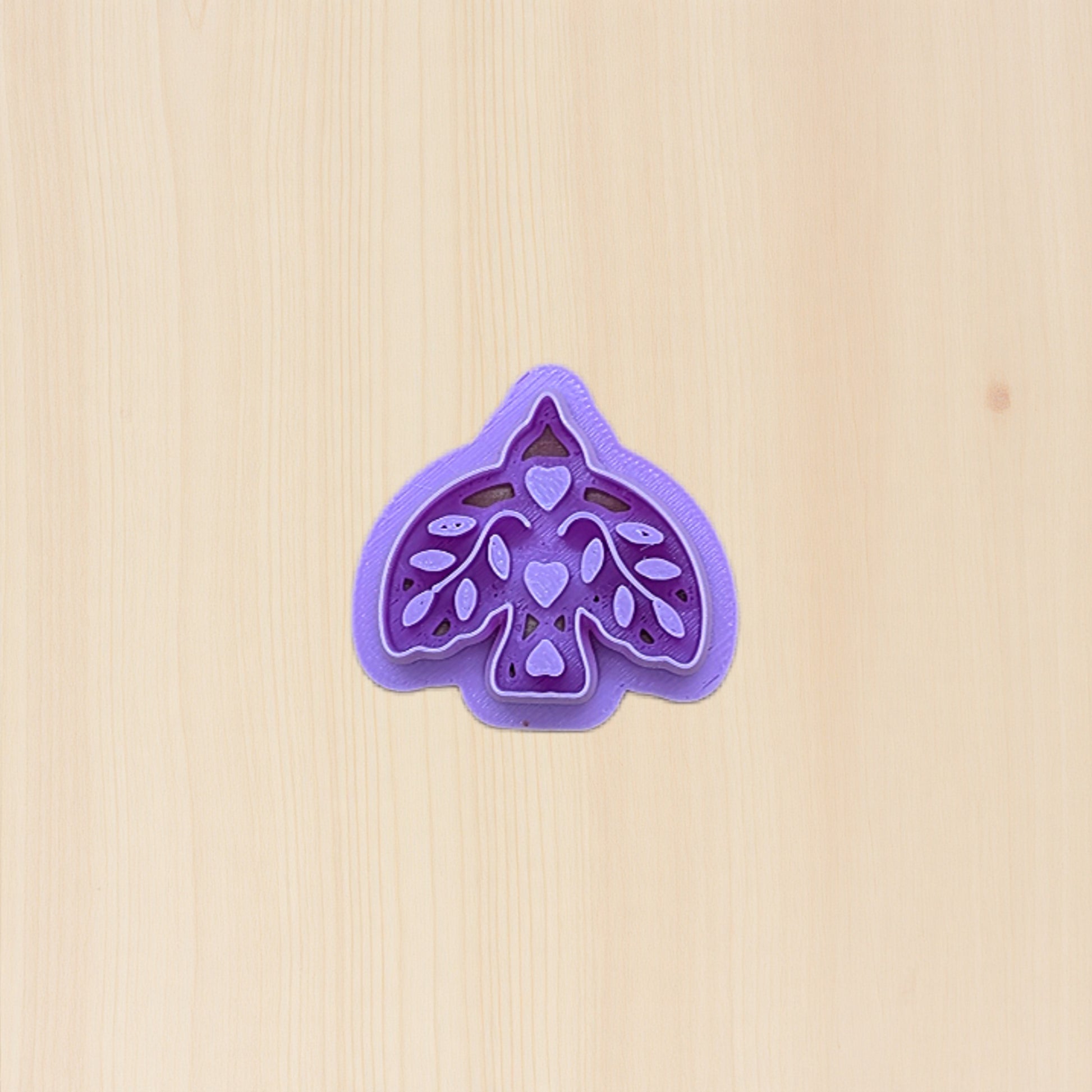 Purple boho bird cookie cutter with folk art design on a birchwood background
