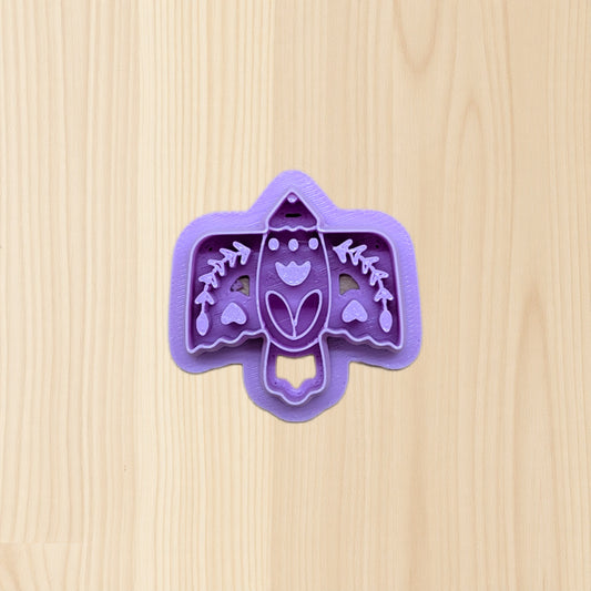 Purple boho folk art bird cookie cutter with bird design on a wooden surface