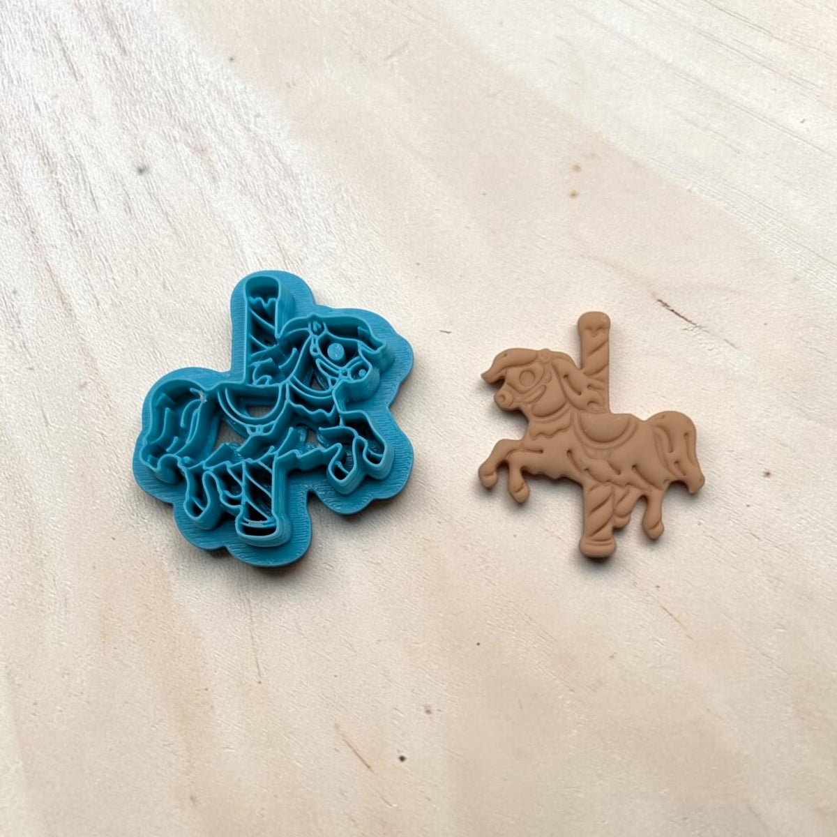 Blue carousel horse cookie cutter beside a tan molded horse figure showing intricate saddle and mane details.