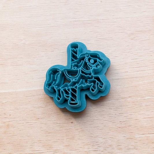 Teal carousel horse cookie cutter with detailed mane, saddle, and pole design on a light wooden surface.