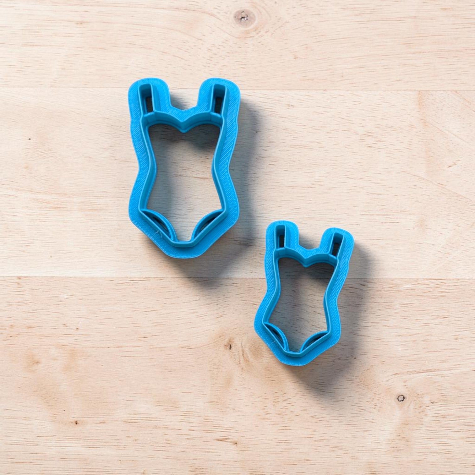Two blue bathing suit-shaped cookie cutters on a wooden surface