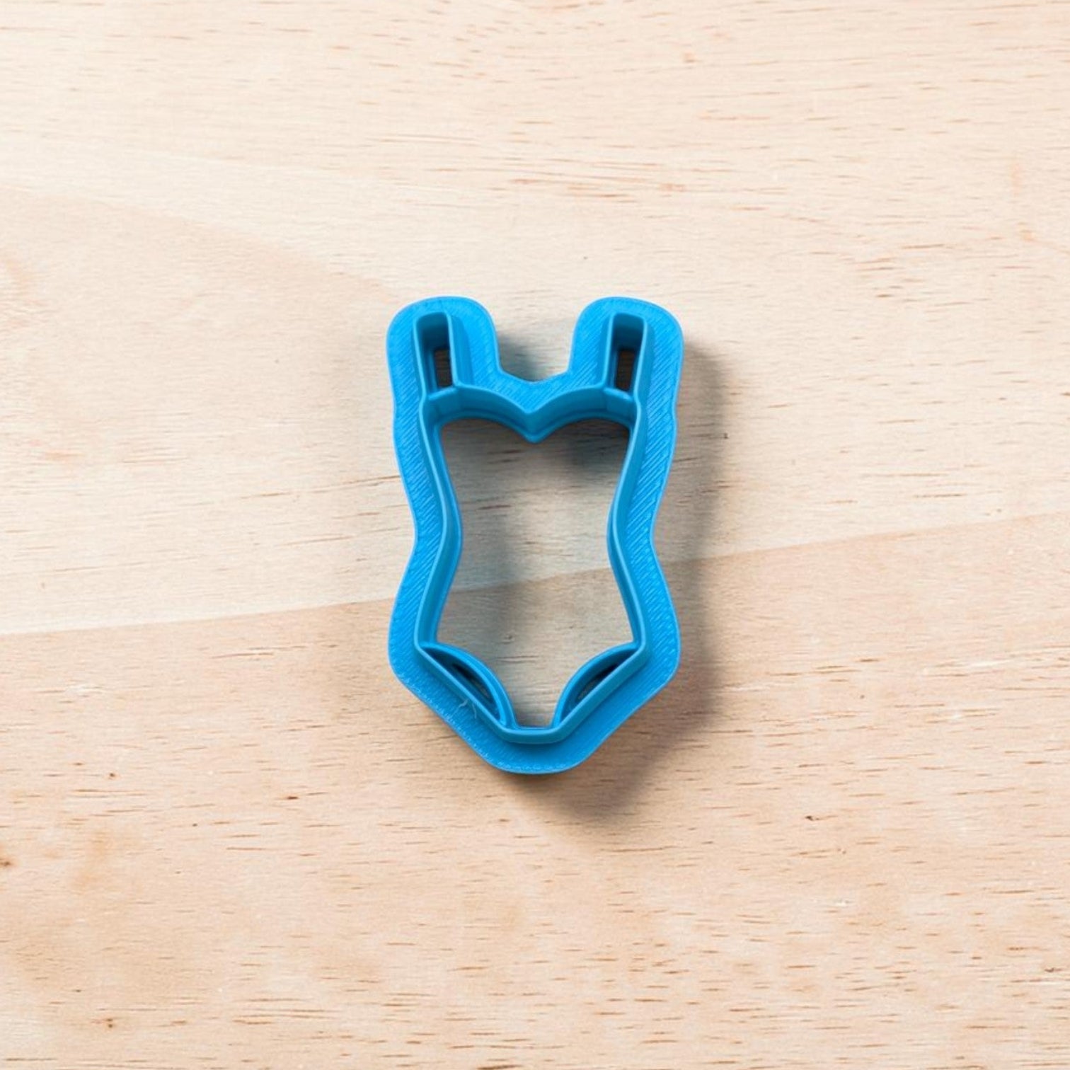 Blue swimsuit-shaped cookie cutter on a wooden surface