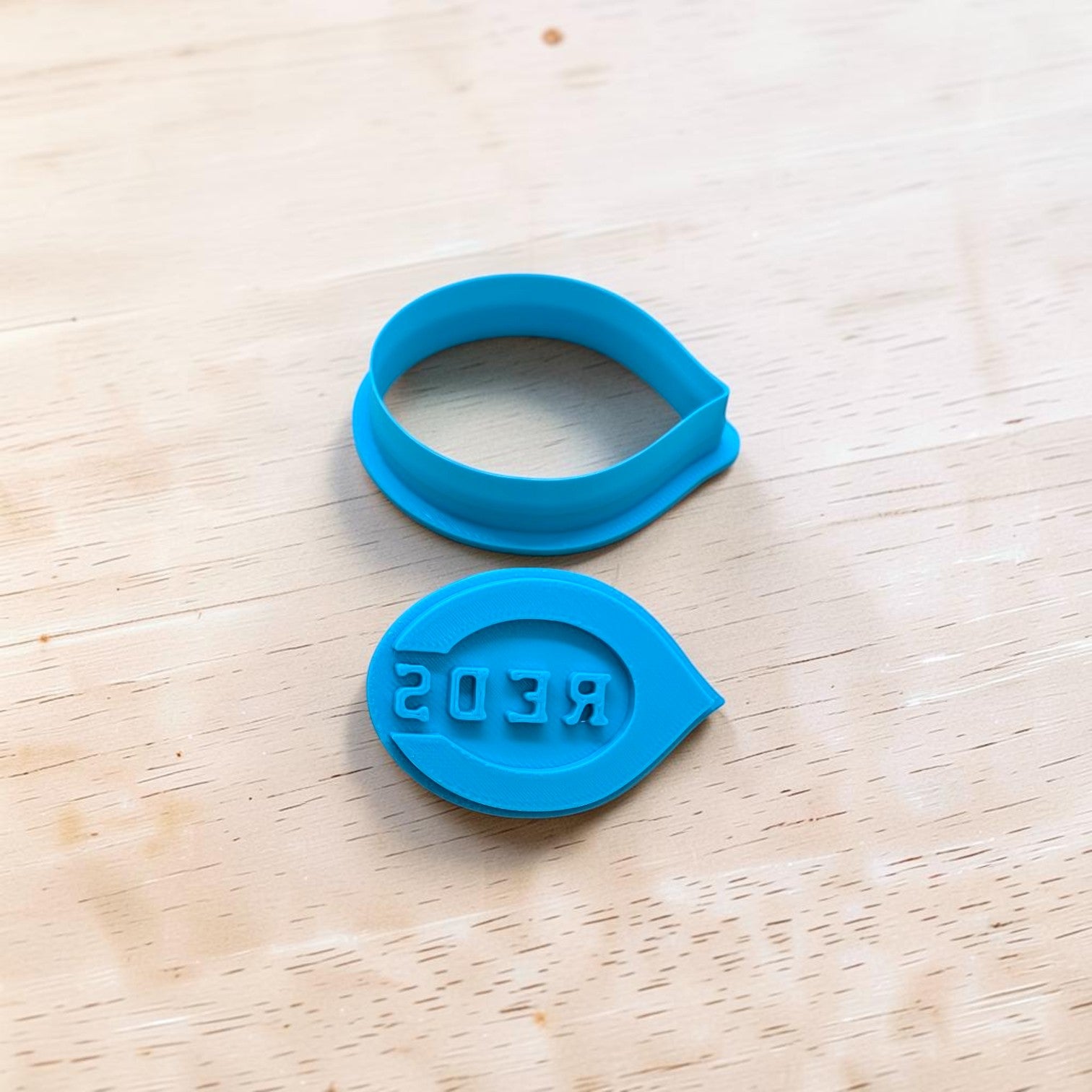 Two blue cookie cutters with 'REDS' printed on them on a wooden surface.