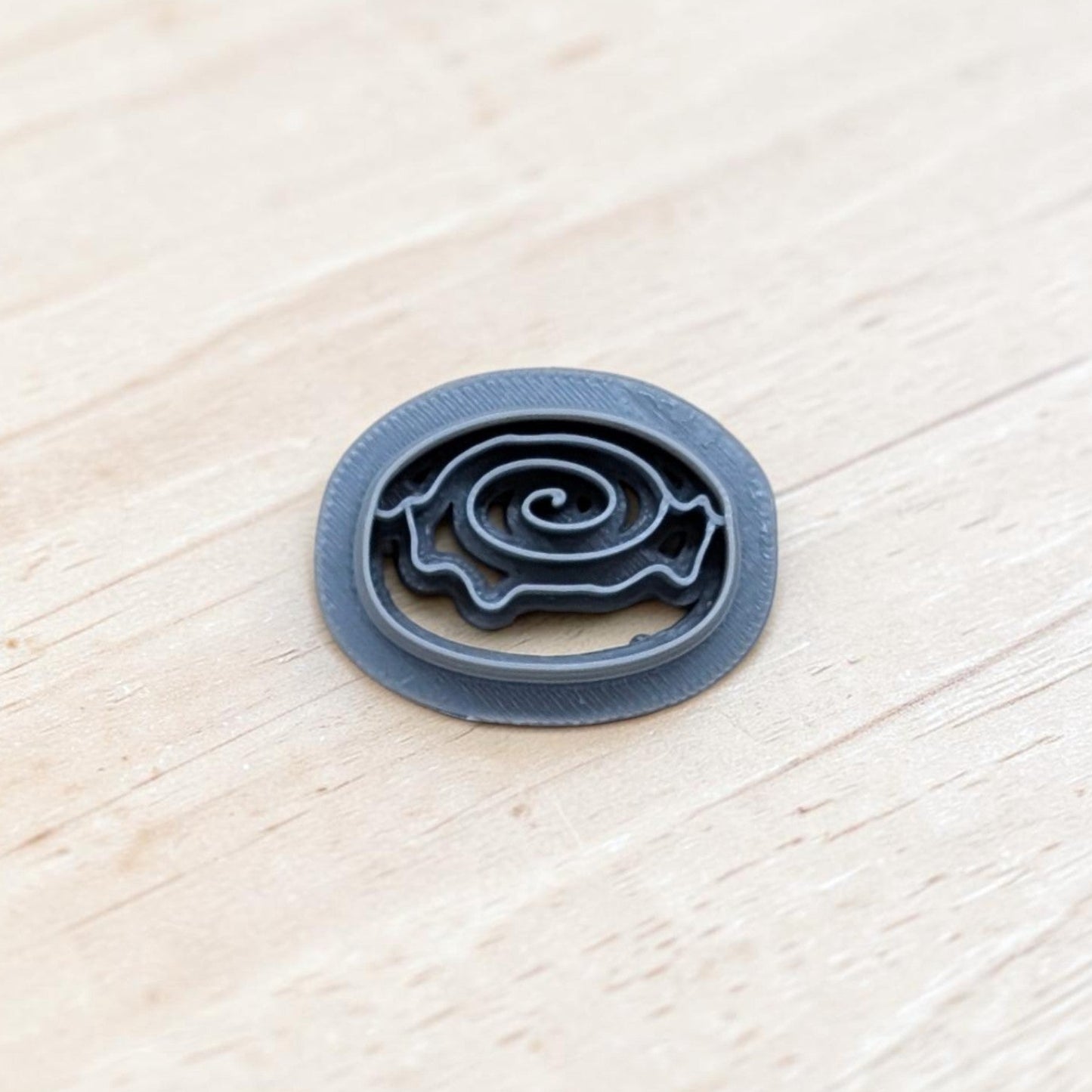 Cinnamon roll cookie cutter with spiral swirl design and smooth rounded edges, displayed on a light wooden surface—perfect for cookies, fondant, polymer clay, and pottery crafts.