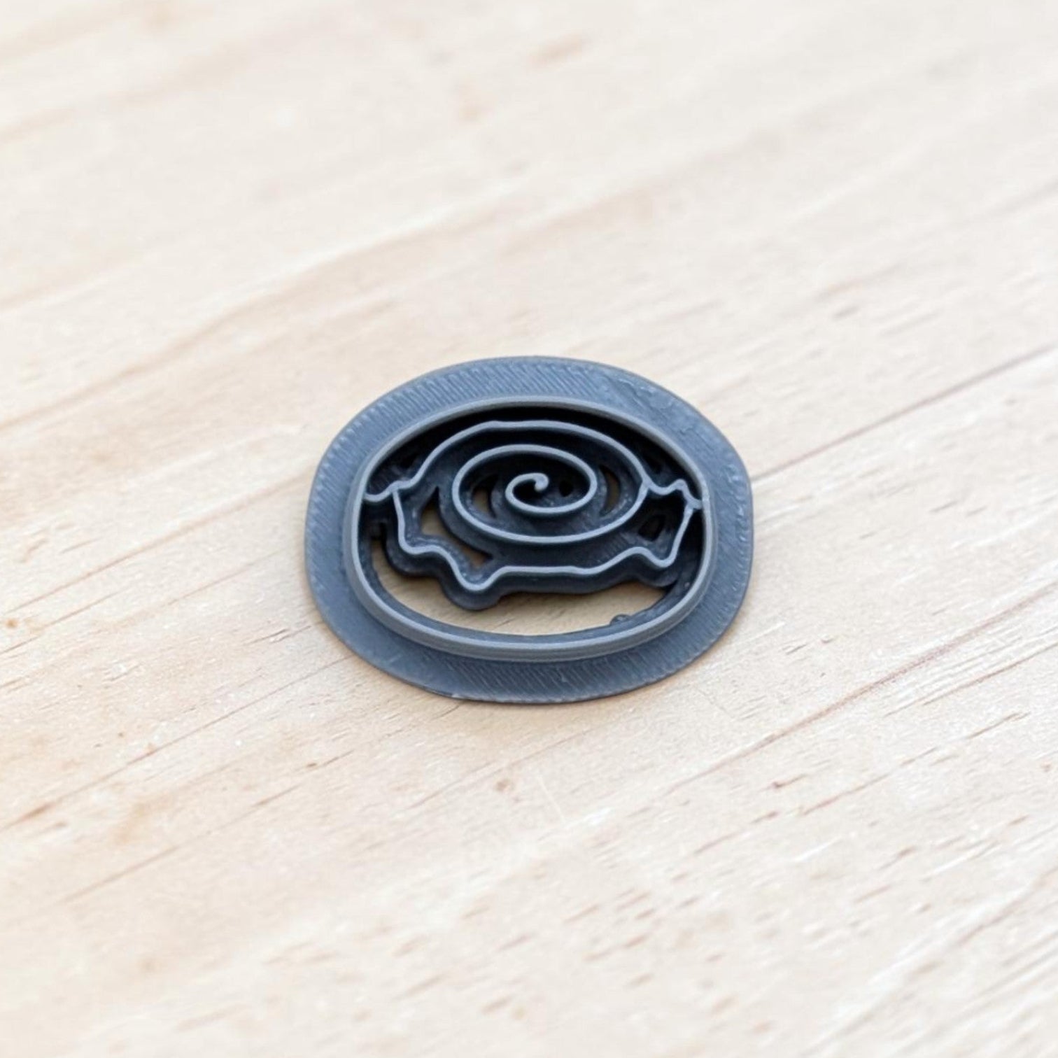 Cinnamon roll cookie cutter with spiral swirl design and smooth rounded edges, displayed on a light wooden surface—perfect for cookies, fondant, polymer clay, and pottery crafts.