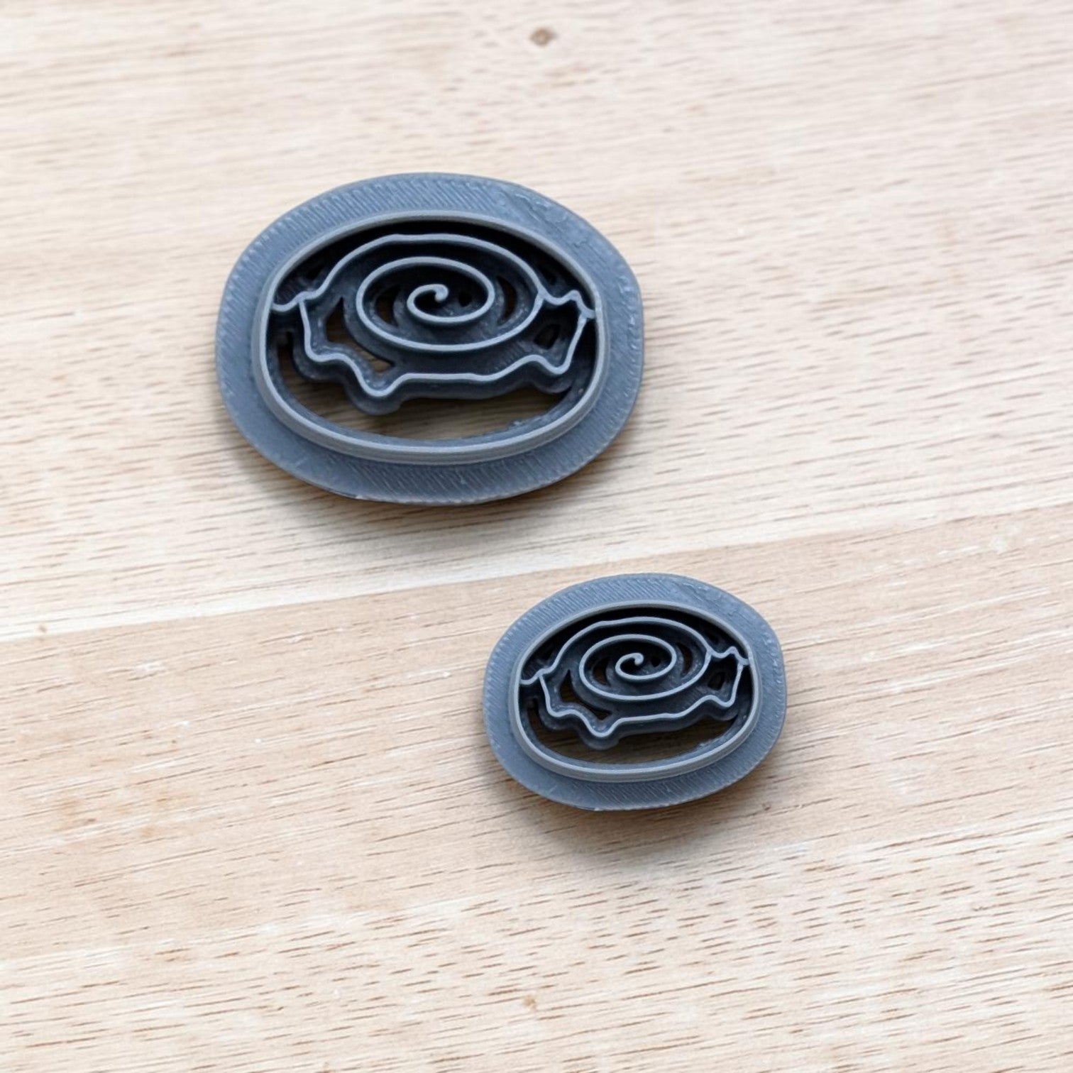 Two cinnamon roll cookie cutters in different sizes with spiral swirl design, displayed on a light wooden surface—perfect for cookies, fondant, polymer clay, and pottery crafts.