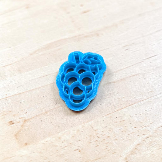 Blue cookie cutter shaped like a cluster of grapes on a light wooden surface