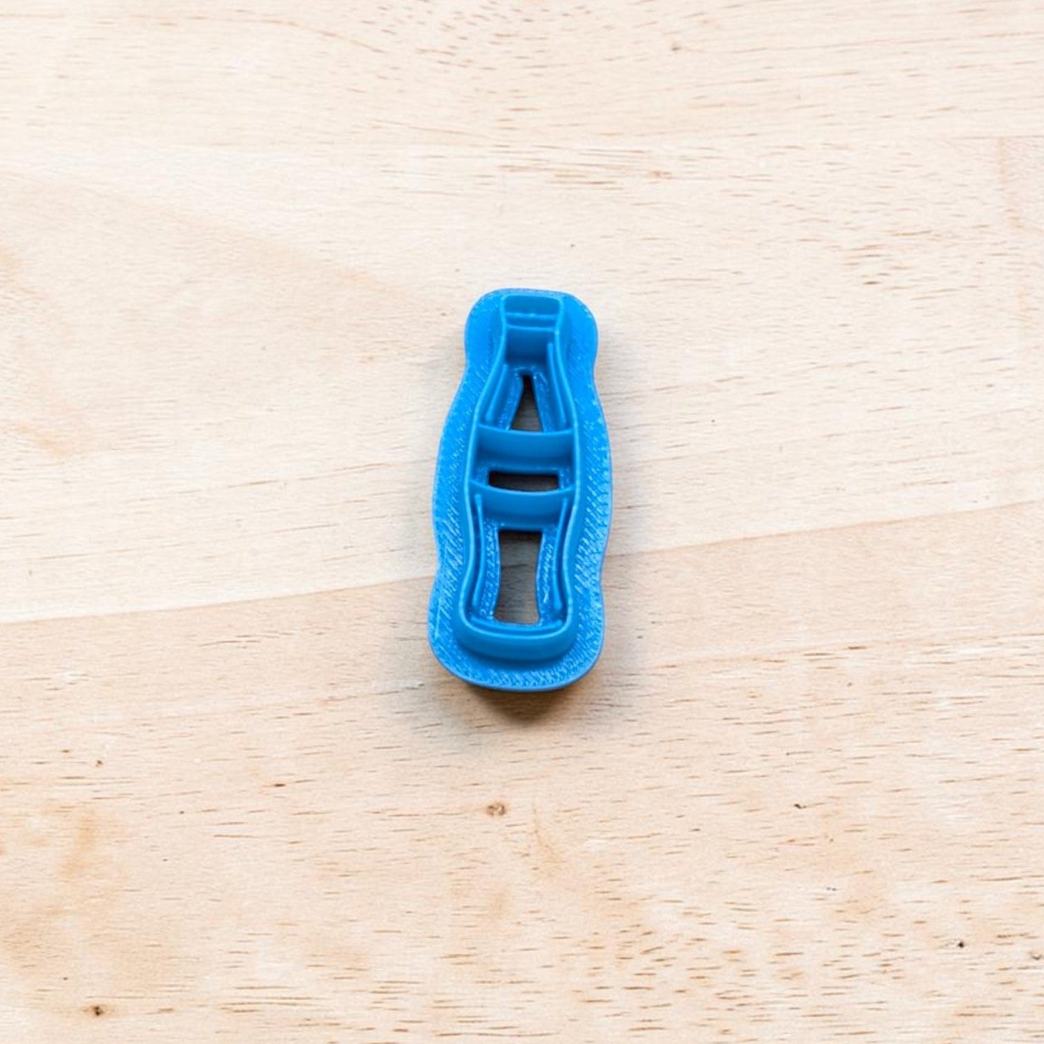 Blue plastic Coke bottle-shaped cookie cutter on a wooden surface