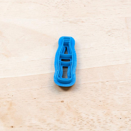 Blue plastic Coke bottle-shaped cookie cutter on a wooden surface