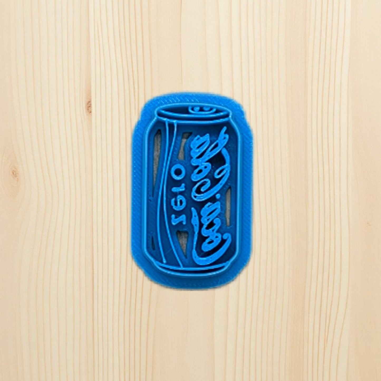 Plastic blue cookie cutter shaped like a Coke Coca-Cola zero soda can on a wooden surface