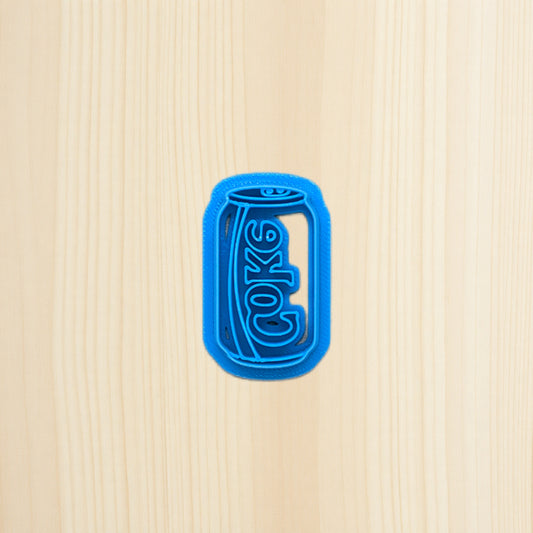 Blue cookie cutter shaped like a soda can with 'Coke' branding on a beige background