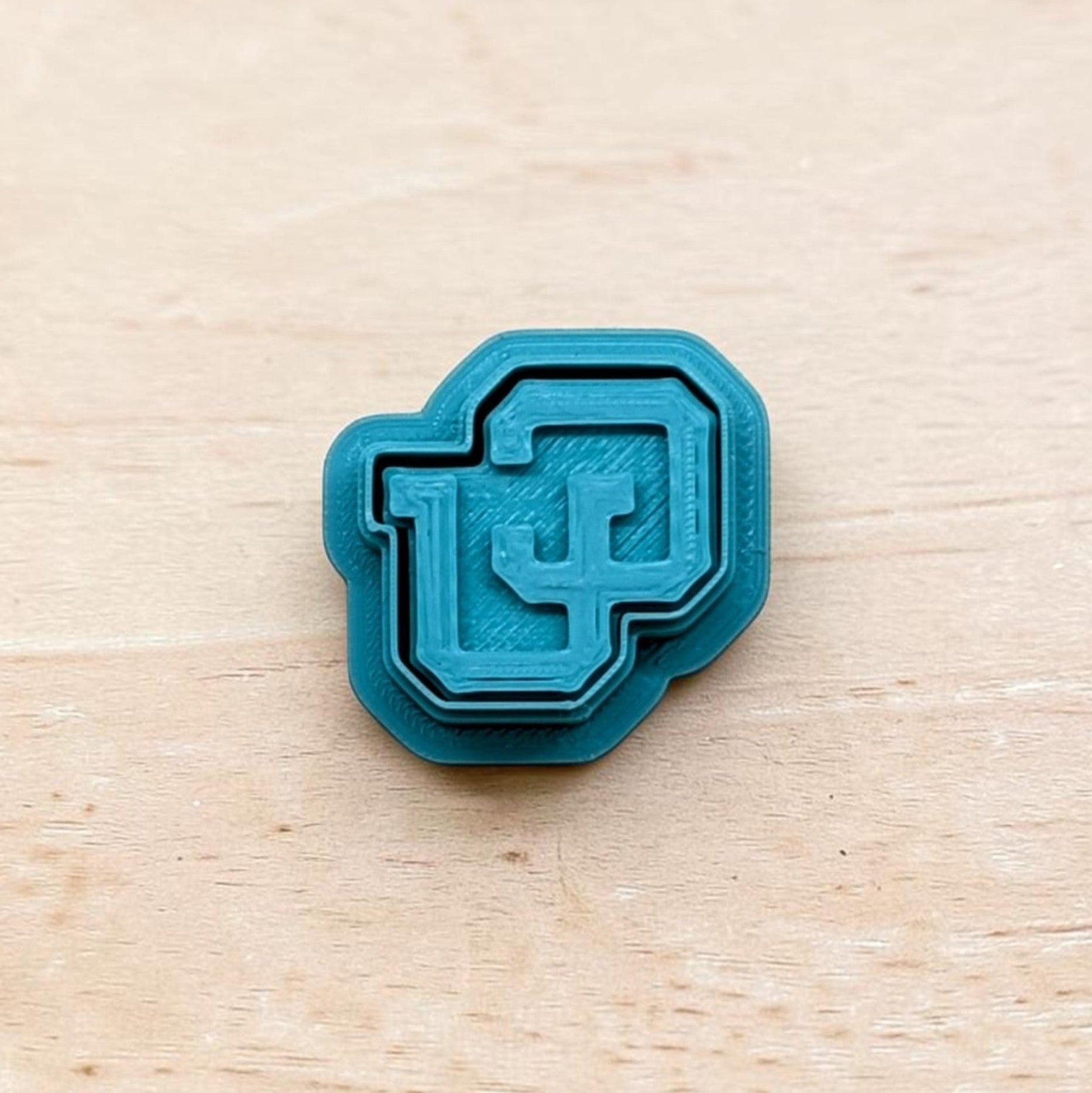 Teal 3D‑printed Colorado Buffaloes CU logo embosser with layered design on light wood background — ideal for cookies, fondant, clay, or pottery detailing.