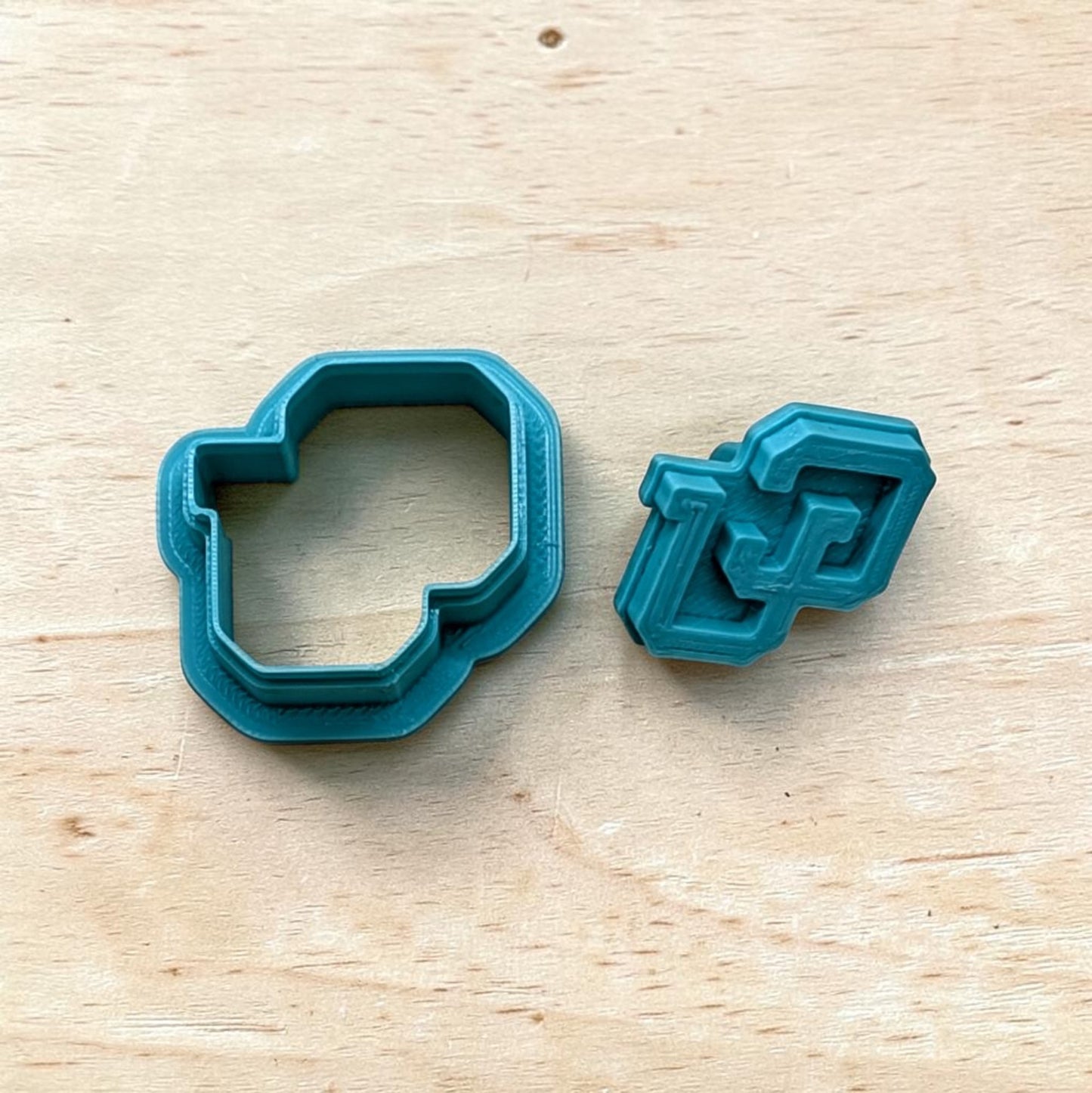 Set of teal 3D‑printed Colorado Buffaloes CU cookie cutter and matching embosser on wooden surface — perfect for polymer clay, fondant, or ceramic crafting.