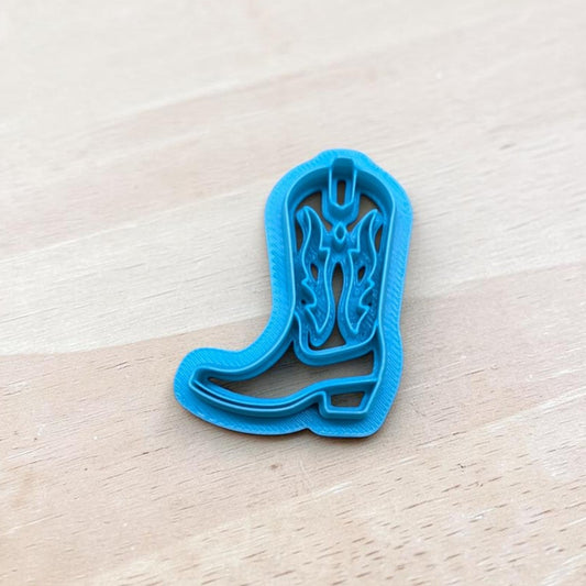 Cowgirl Boot Cookie Cutter – blue 3D printed western boot polymer clay and fondant cutter with detailed stitching design on wooden background.