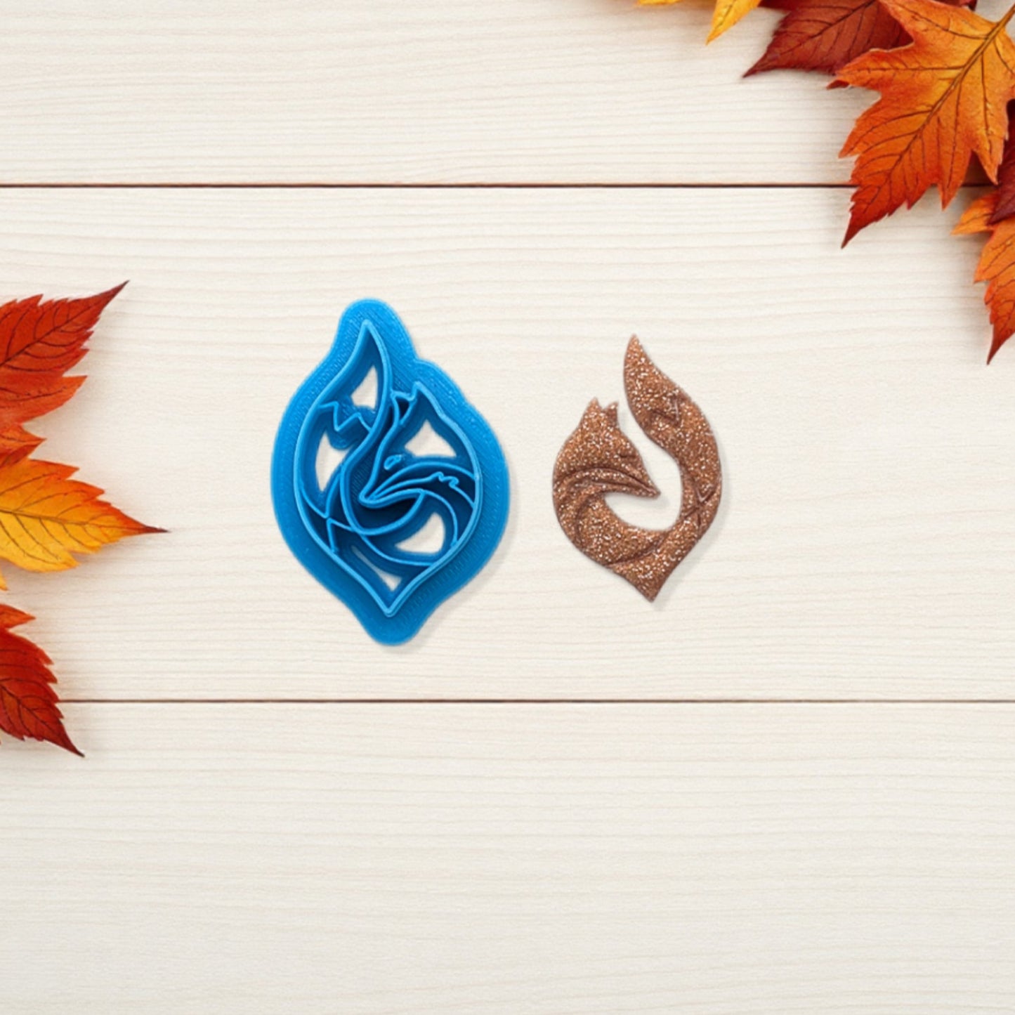 Blue and brown leaf-shaped cookie cutters on a wooden surface with autumn leaves.